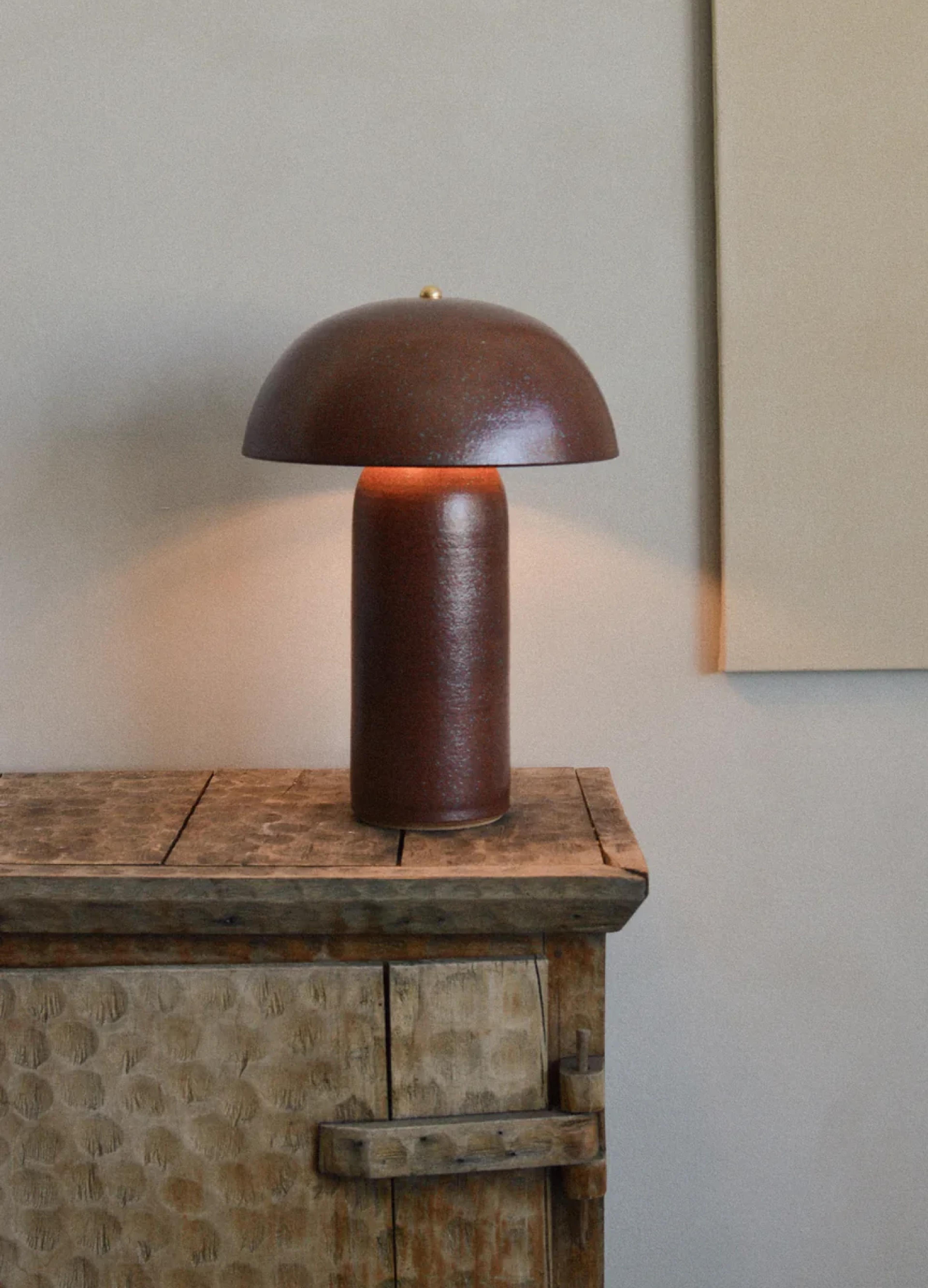 A sleek, brown lamp with a rounded shade sits atop a rustic wooden table, illuminated softly against a neutral wall.