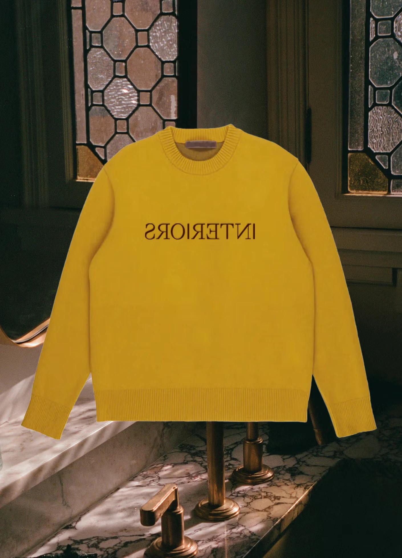 Bright yellow sweater with "INTERIORS" printed in black, displayed against a backdrop of stained glass and marble.