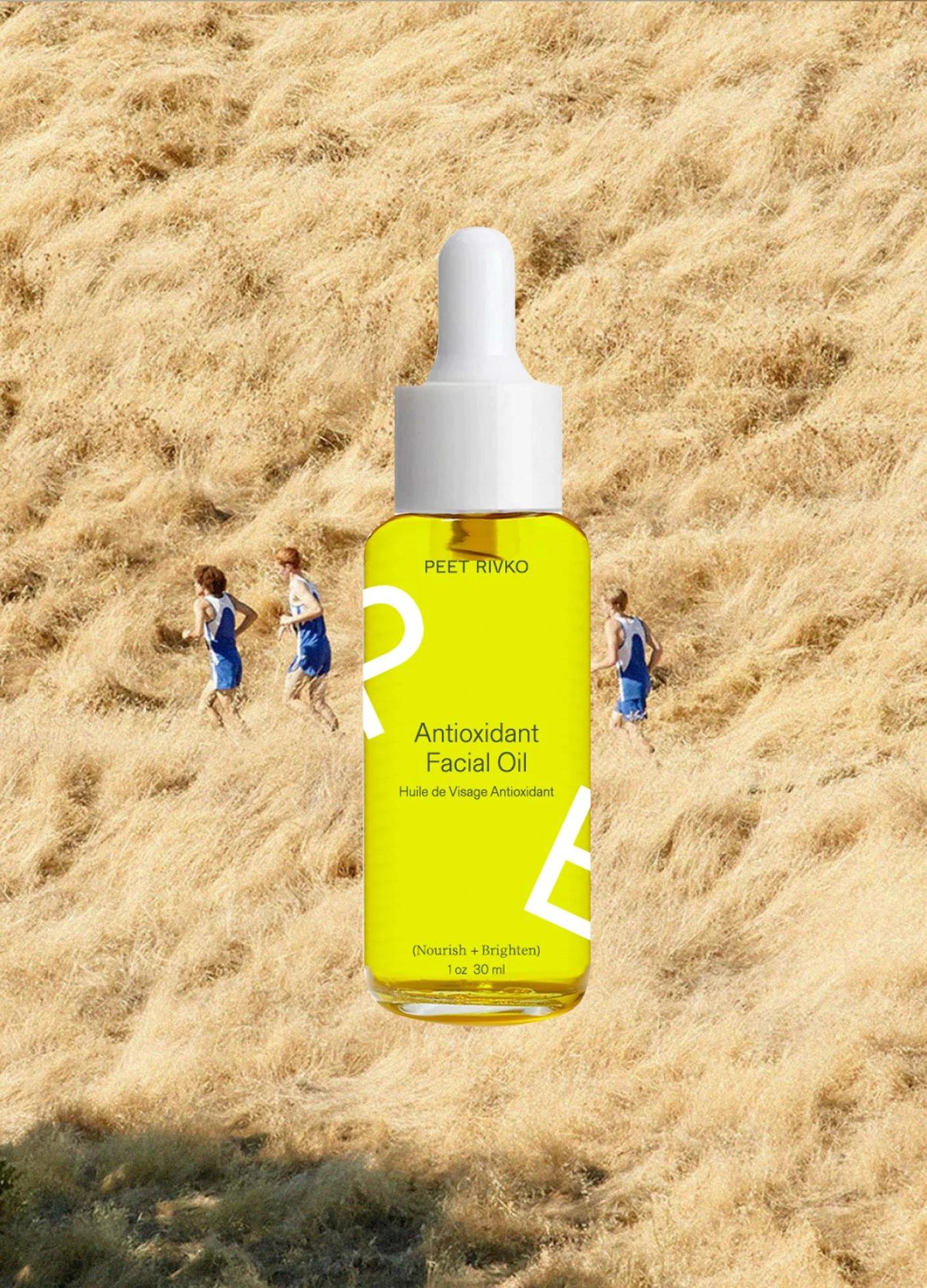 Bright yellow bottle of Antioxidant Facial Oil in front of two people running on a grassy hillside.