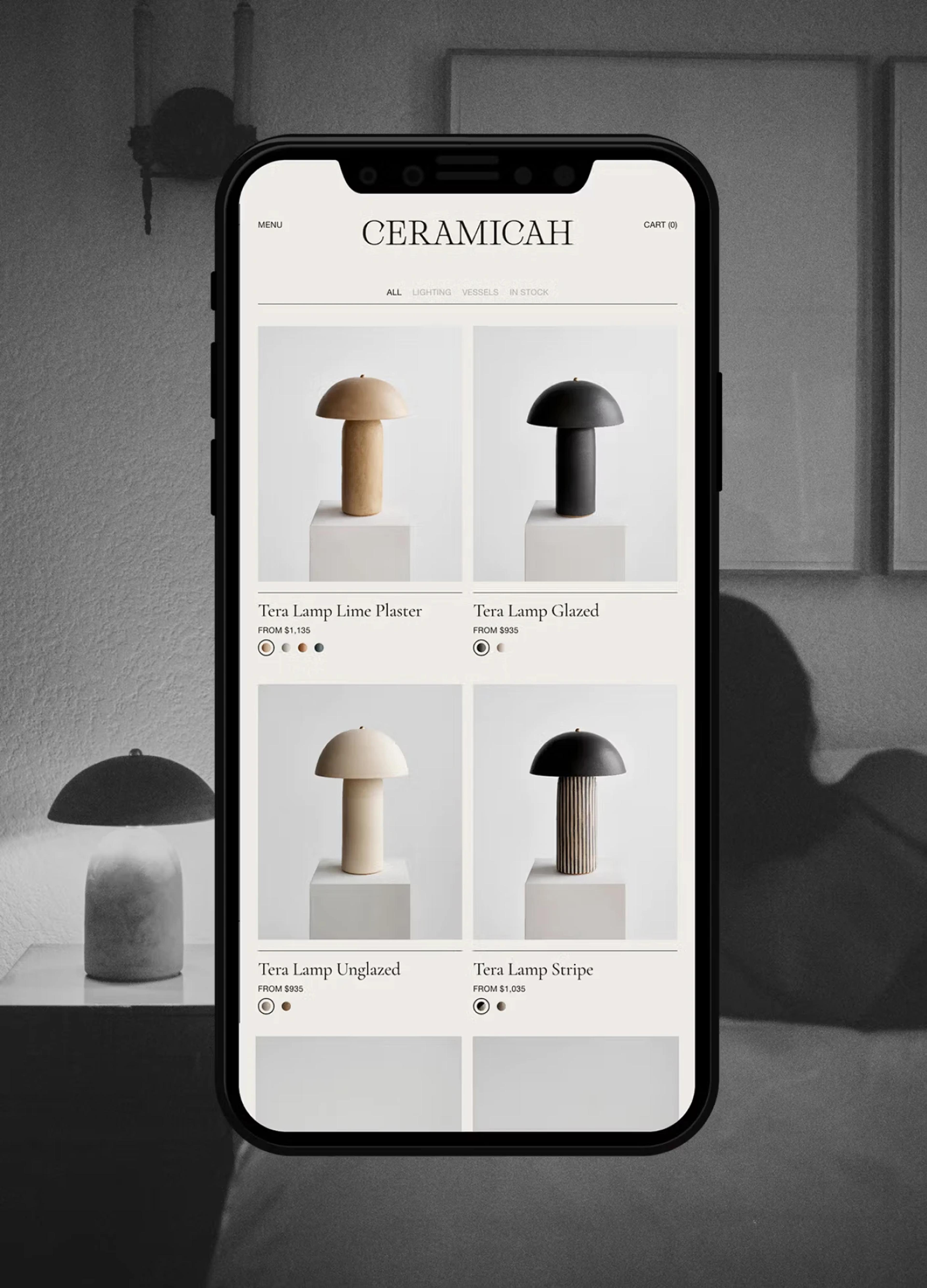 A smartphone displays a selection of ceramic lamps in various styles and colors on a minimalist website.