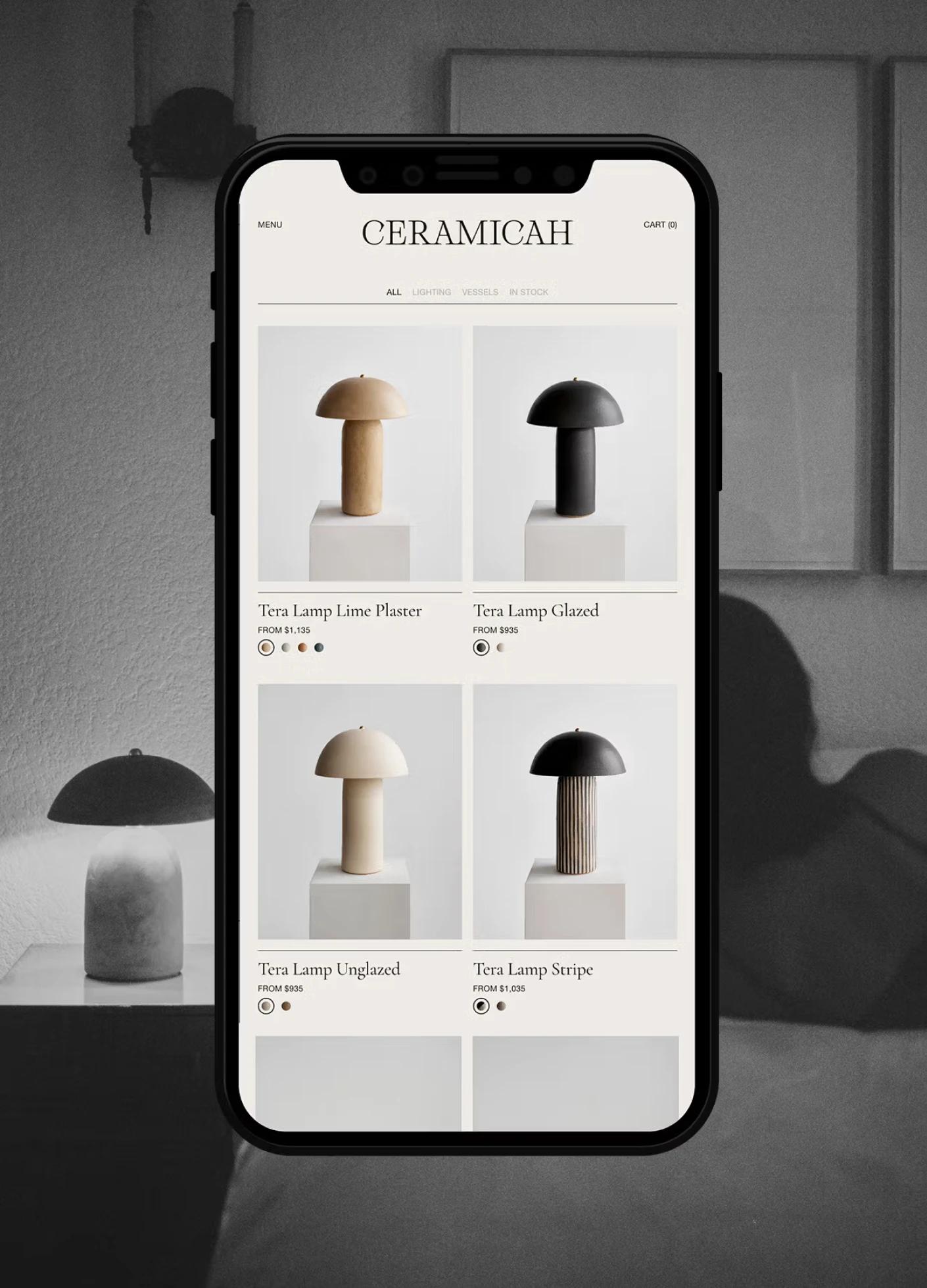 A smartphone displays a selection of ceramic lamps in various styles and colors on a minimalist website.