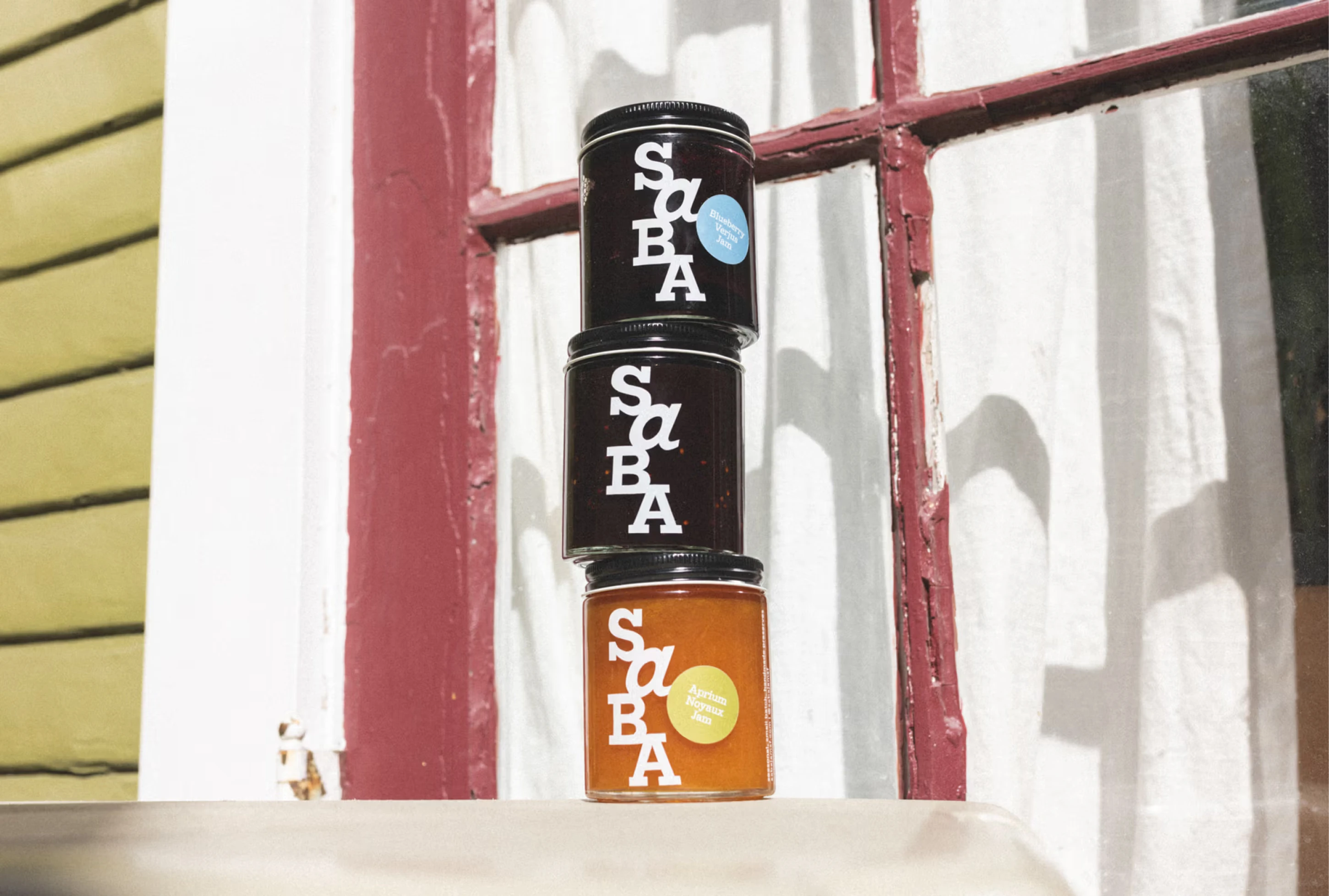 Three jars of jam stacked in front of a window, featuring bold SBA branding and a yellow label on the bottom jar.