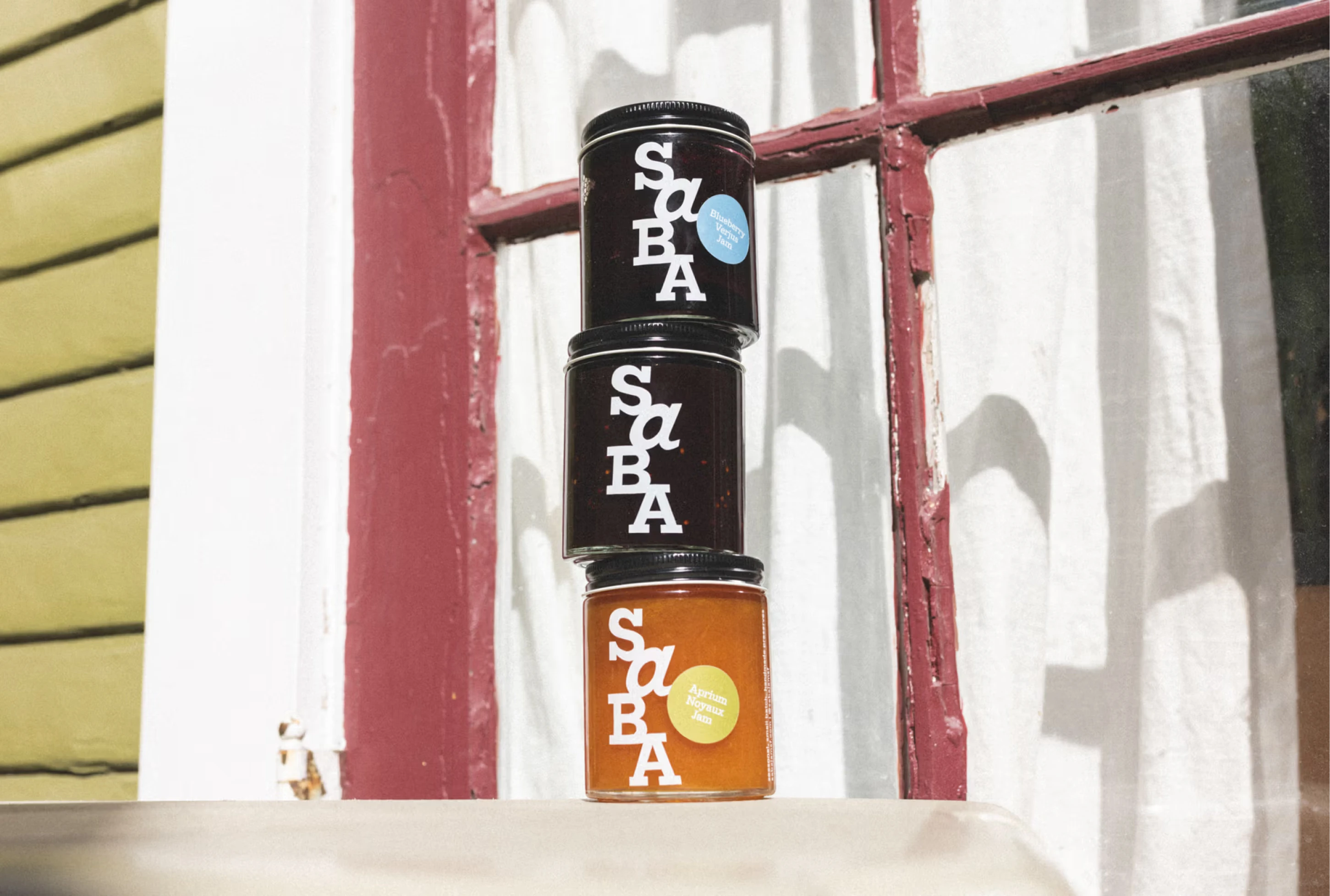Three jars of jam stacked in front of a window, featuring bold SBA branding and a yellow label on the bottom jar.