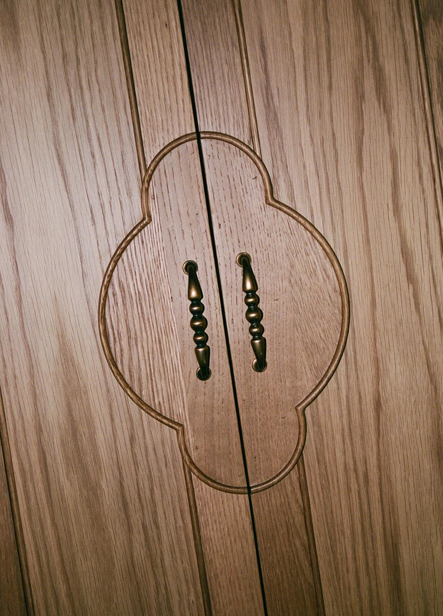 Close-up of wooden cabinet doors with intricate carvings and decorative bronze handles.