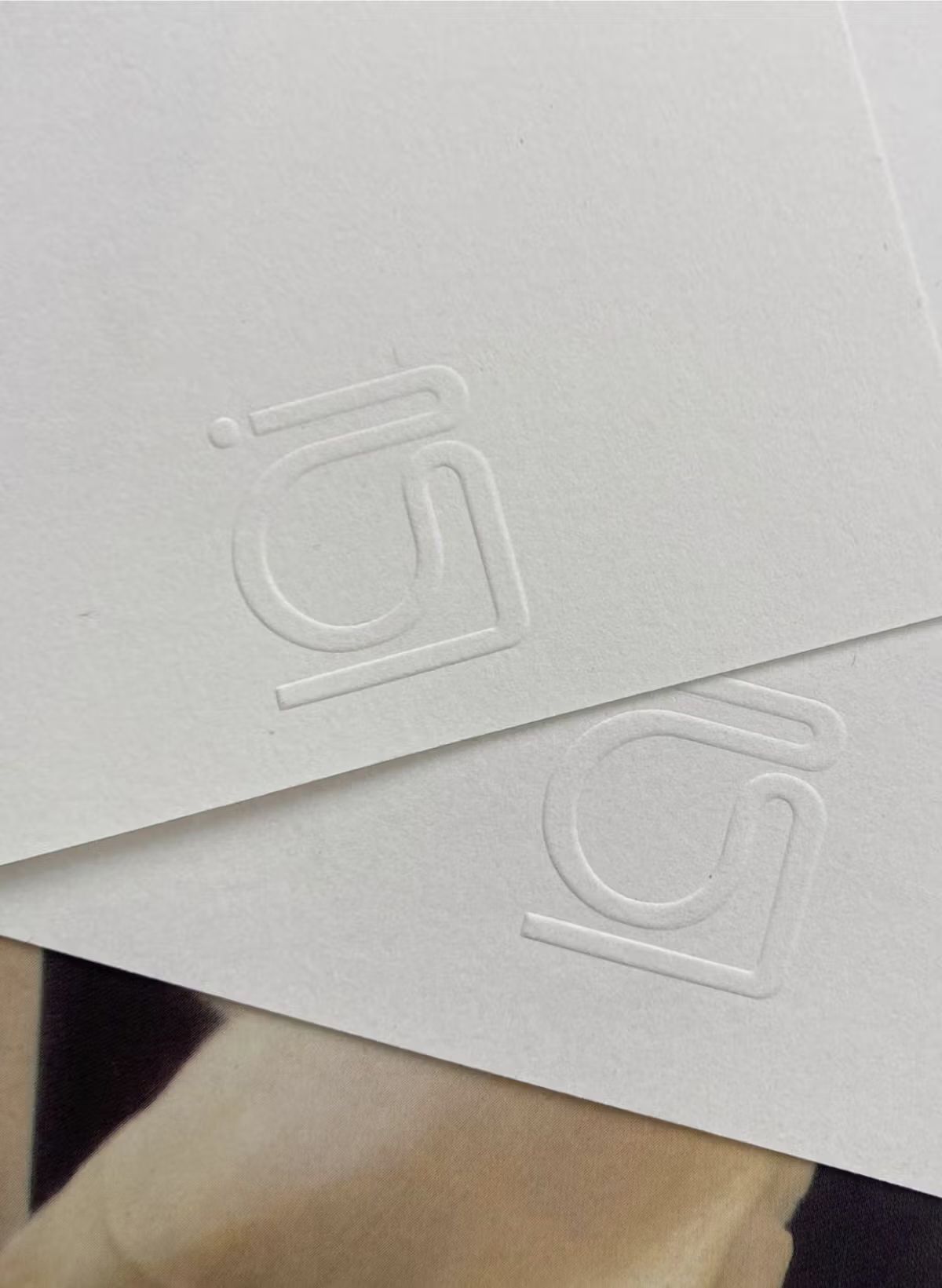 Two white cards with embossed logos partially overlapping, resting on a textured surface.