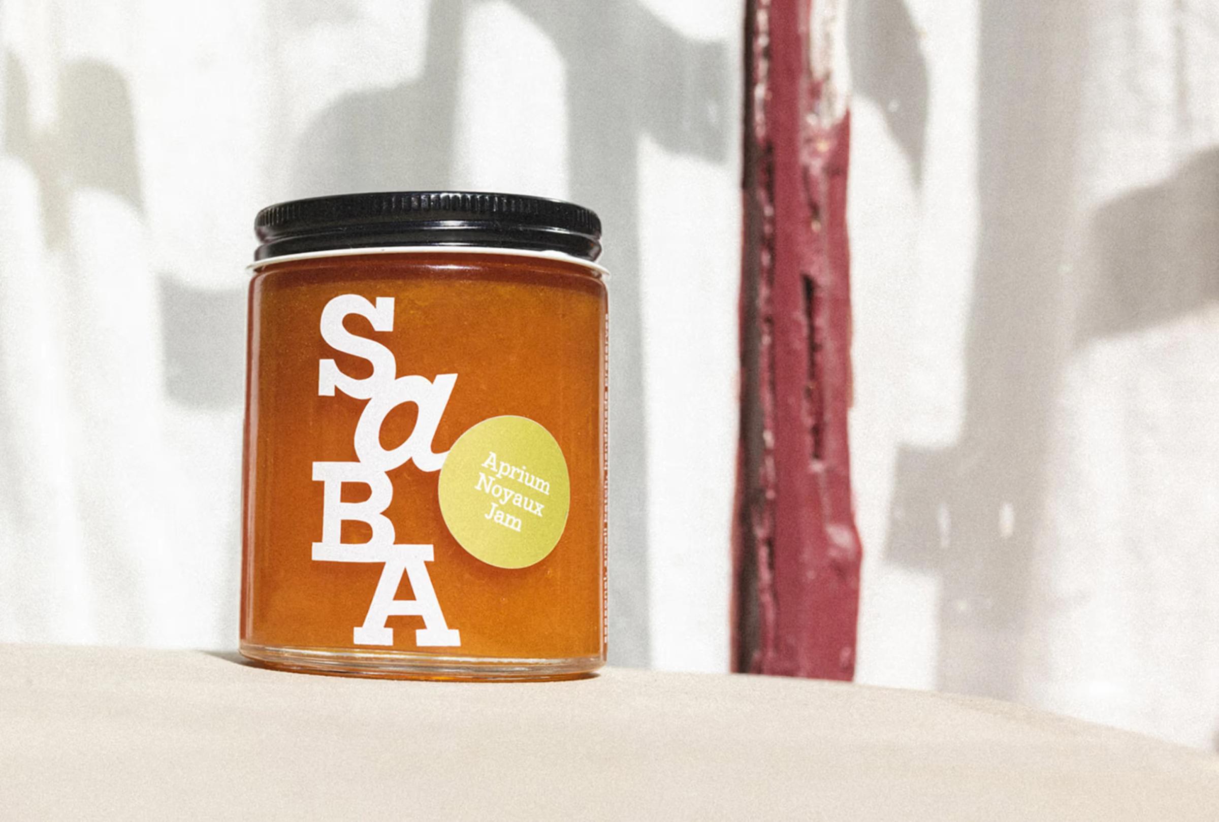 A jar of aprium noyaux jam with a white label featuring bold letters and a yellow sticker, placed on a neutral surface.