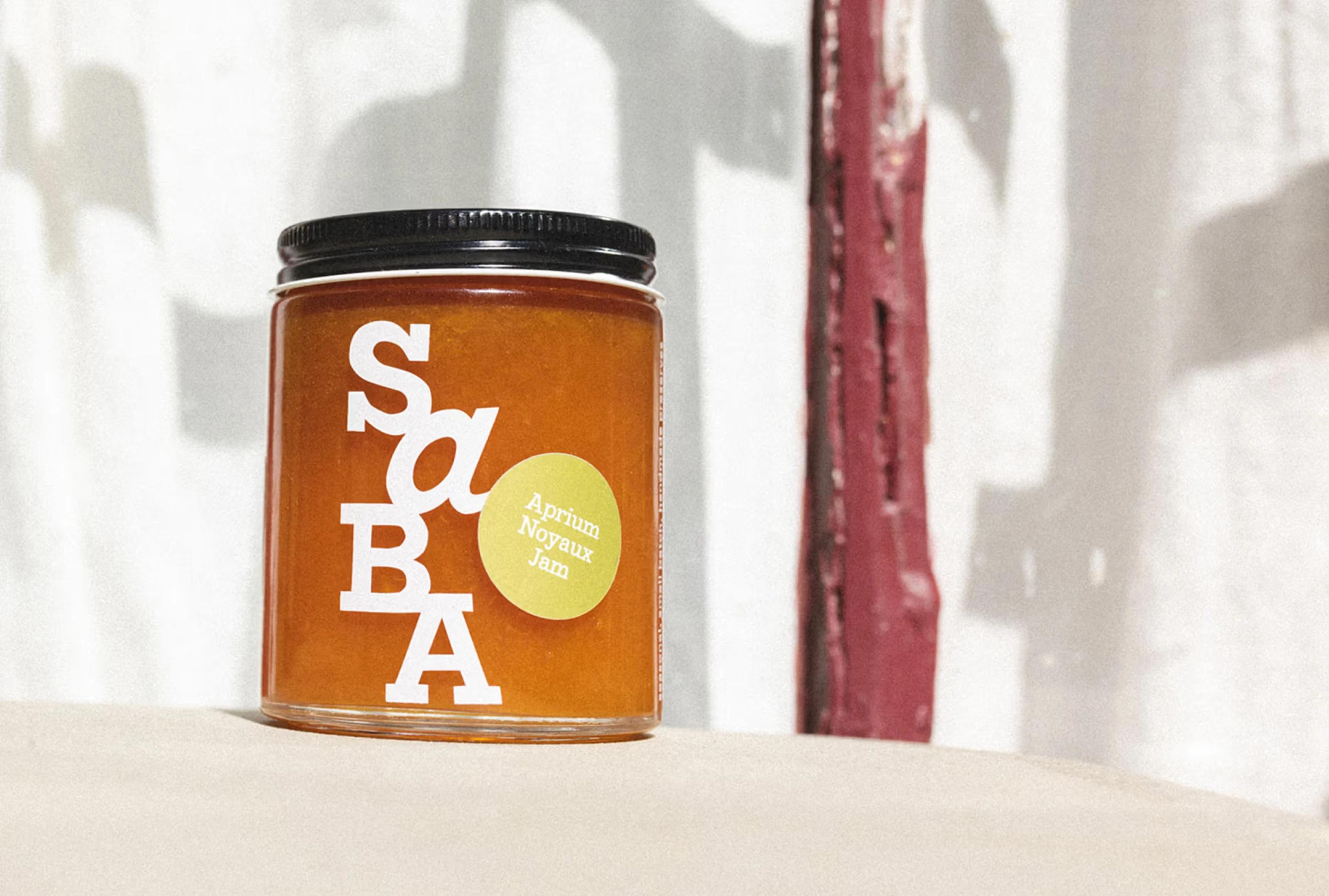 A jar of aprium noyaux jam with a white label featuring bold letters and a yellow sticker, placed on a neutral surface.