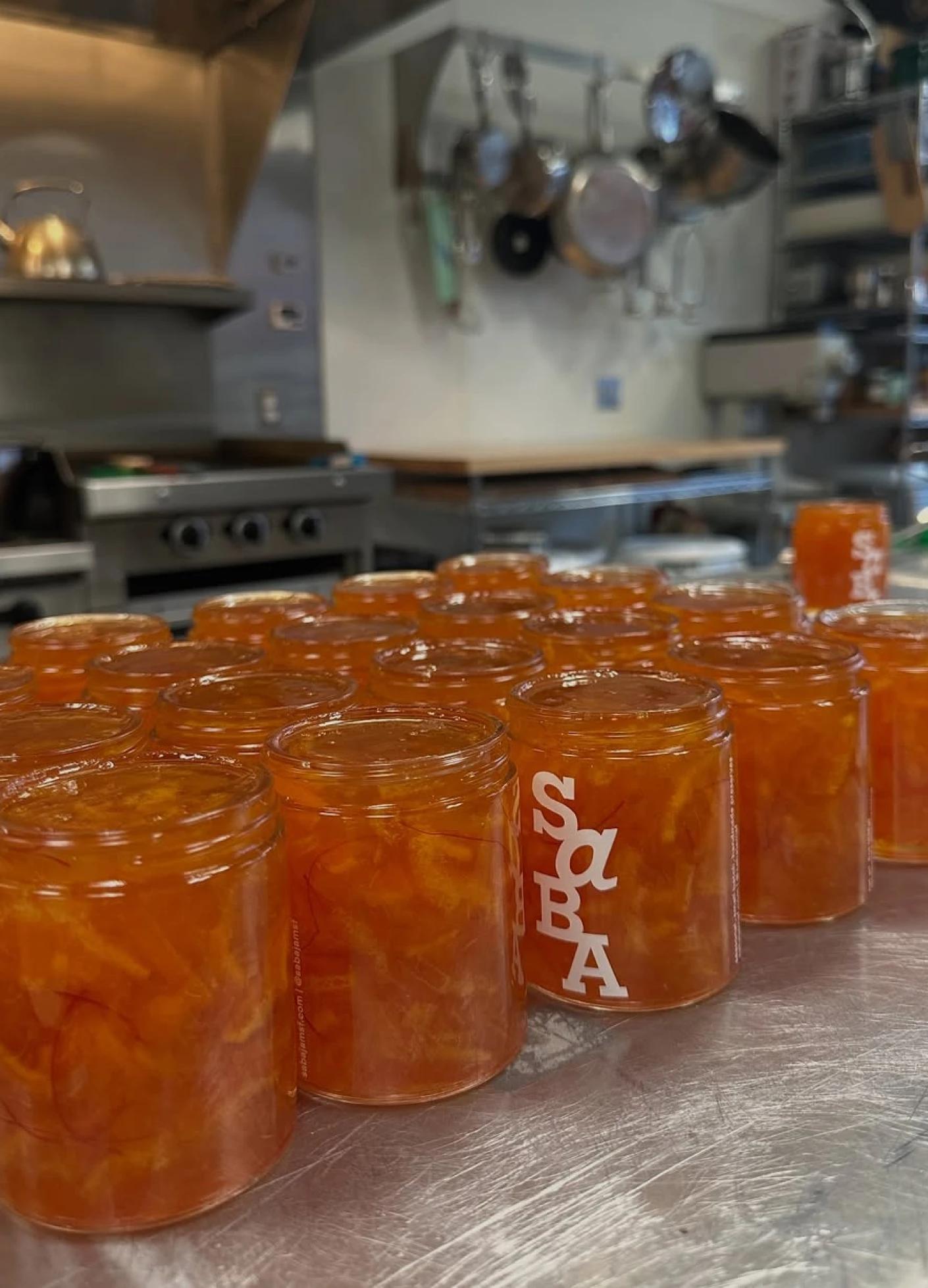 Small glass jars filled with orange jam are arranged on a countertop in a commercial kitchen.