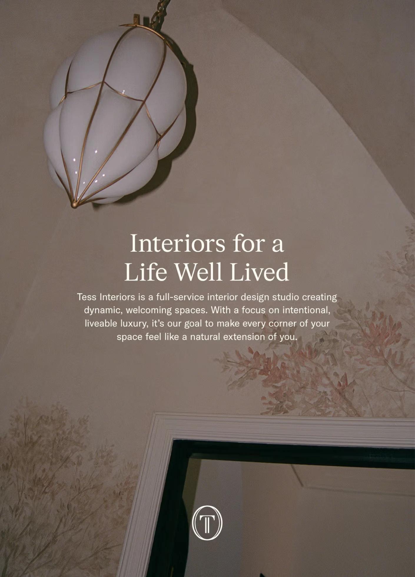 A stylish light fixture hangs from a ceiling, with soft floral wall decor and a mirror reflecting a welcoming interior space.