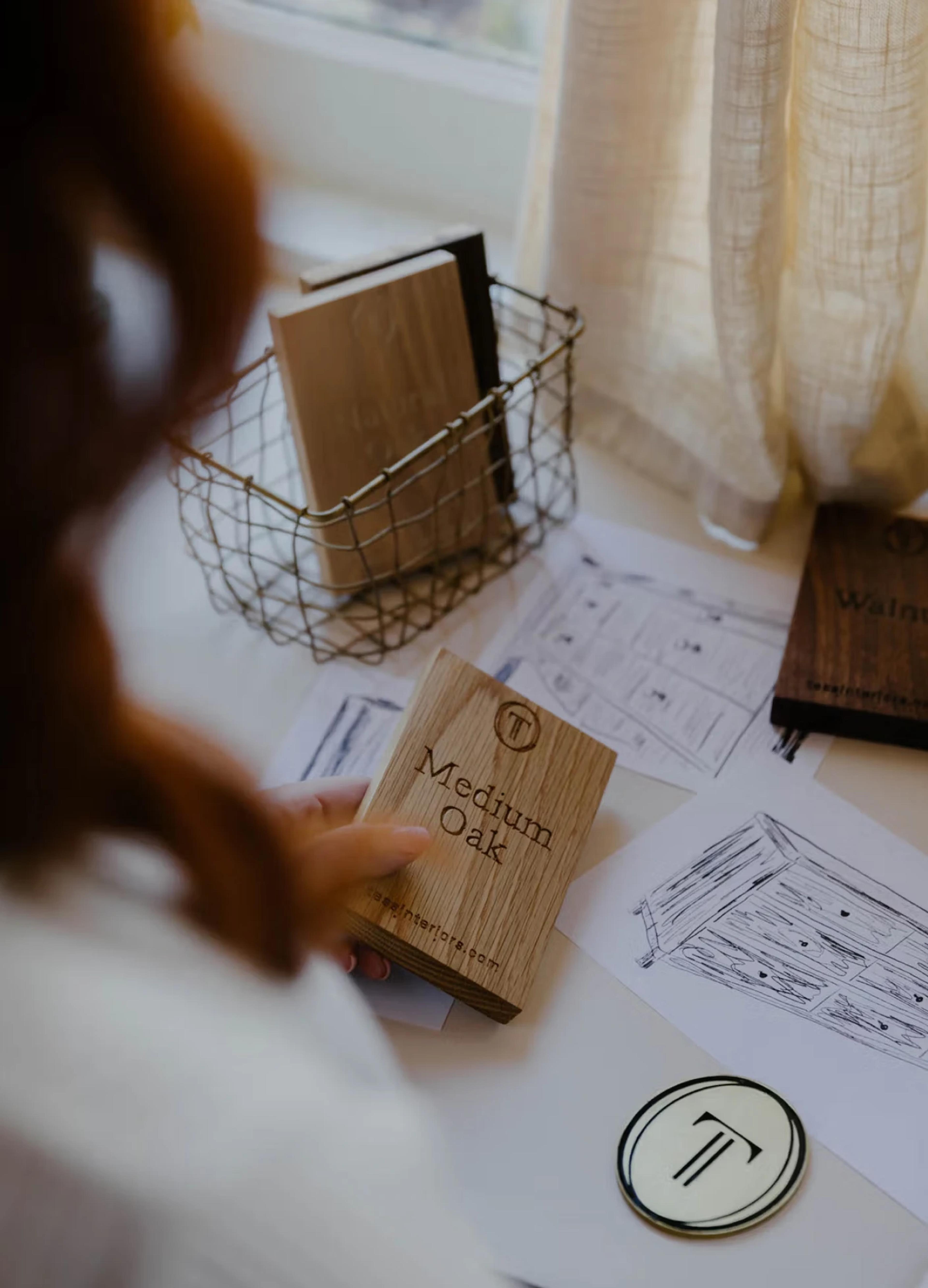 Wood samples labeled "Medium Oak" and "Walnut" alongside design sketches on a table near a window.