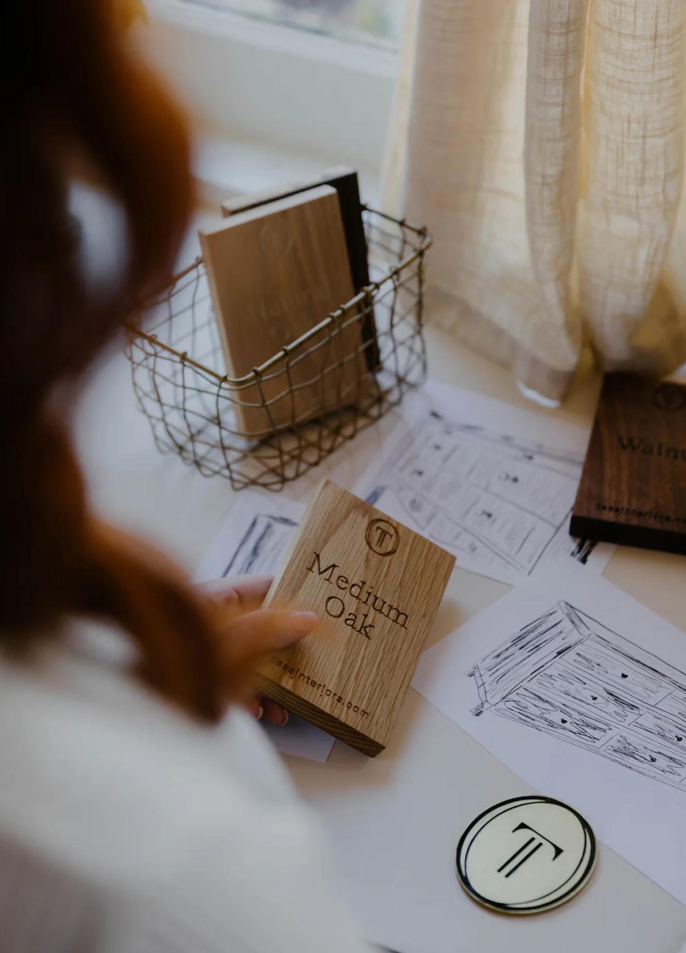 Wood samples labeled "Medium Oak" and "Walnut" alongside design sketches on a table near a window.