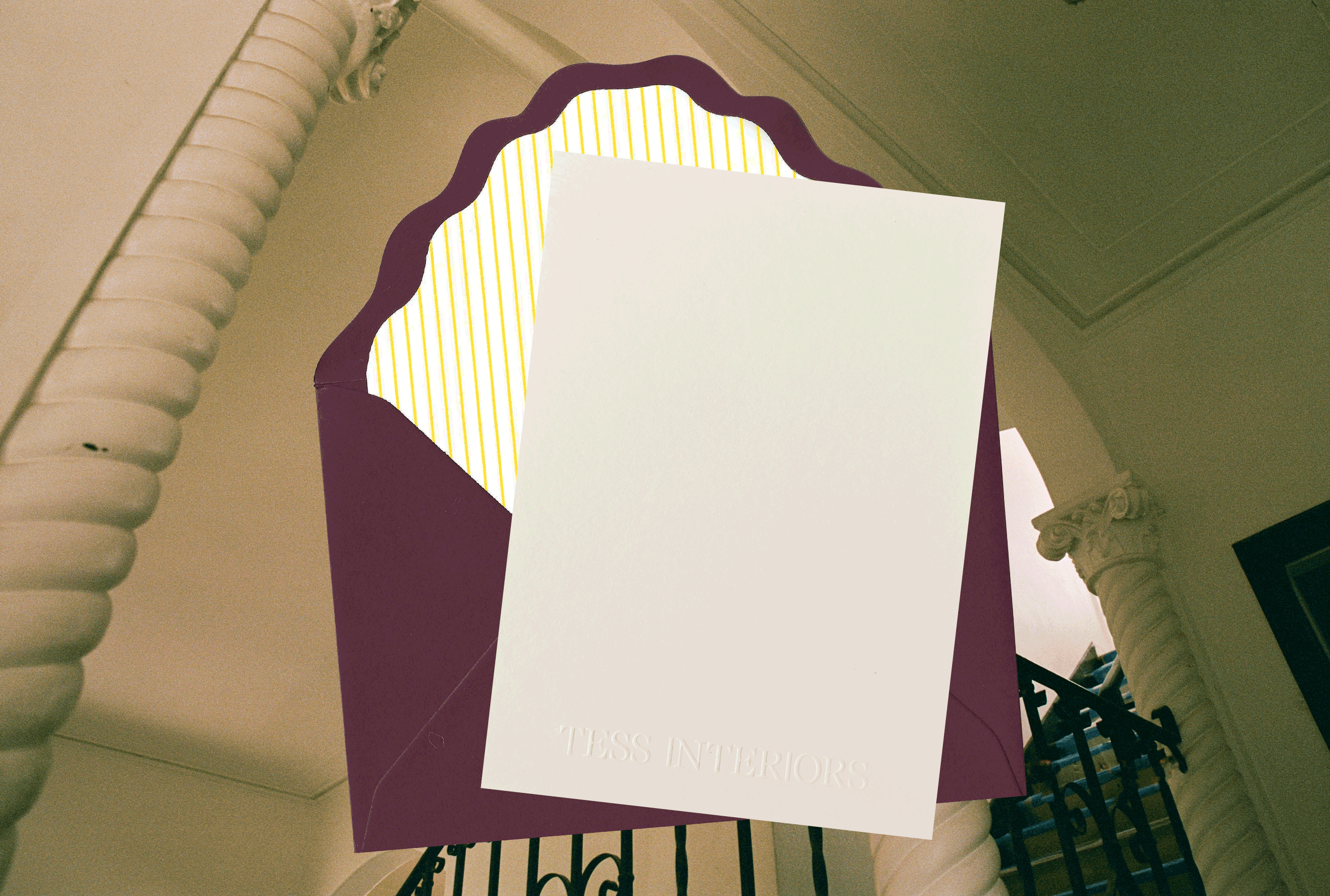 A maroon envelope with a striped yellow interior showcases a blank white card embossed with "TESS INTERIORS."