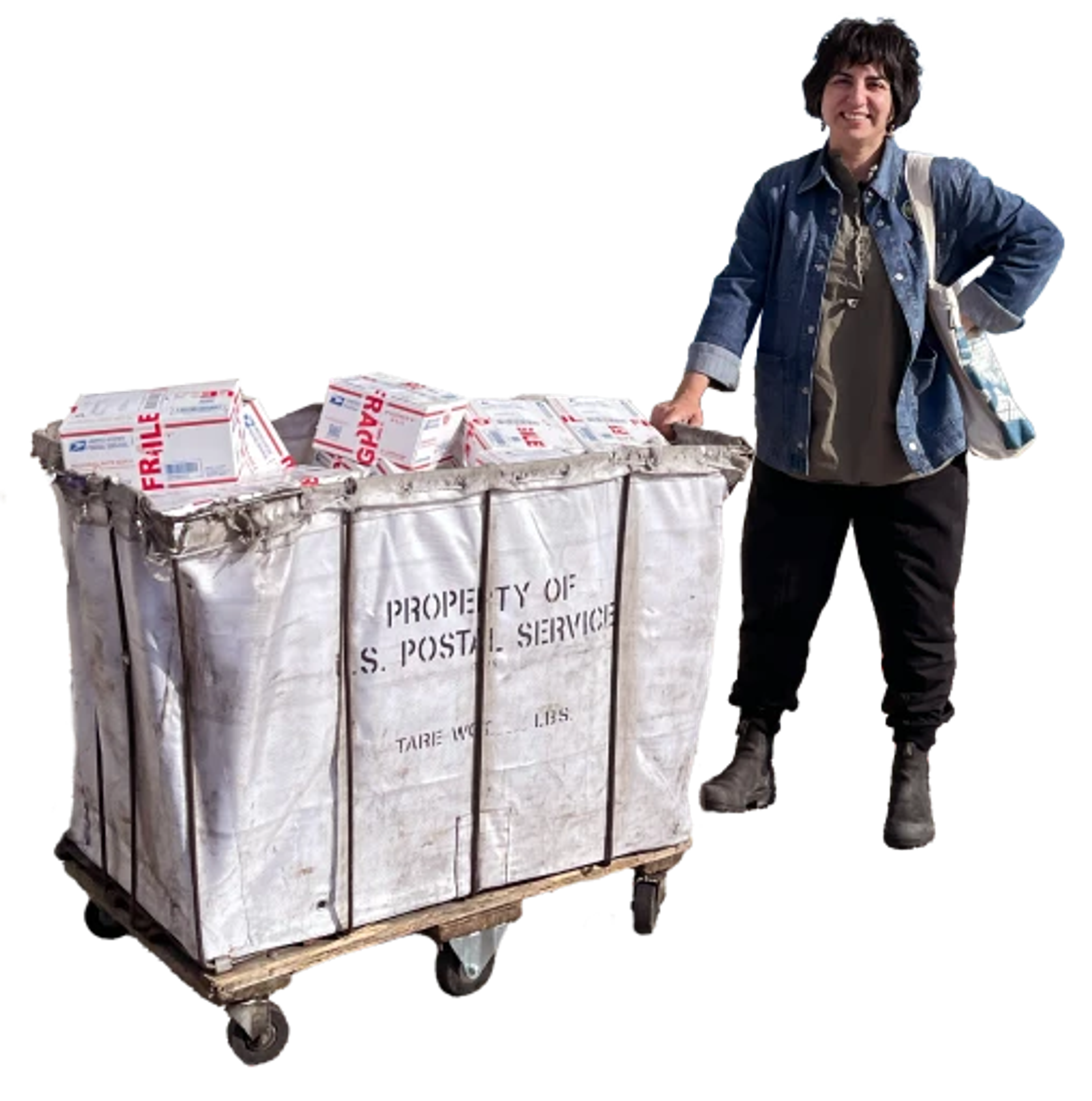 A person stands beside a large postal cart filled with packages, wearing casual clothes and a tote bag.