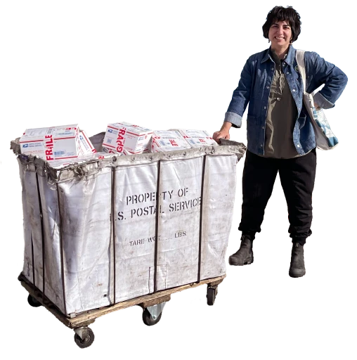 A person stands beside a large postal cart filled with packages, wearing casual clothes and a tote bag.
