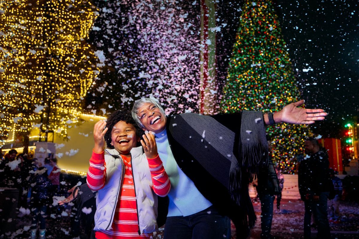 A guest and child laughing under falling snow at Six Flags Holiday in the Park