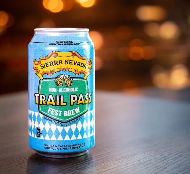 A can of non-alcoholic Trail Pass Fest Brew on a table with blurred lights in the background.