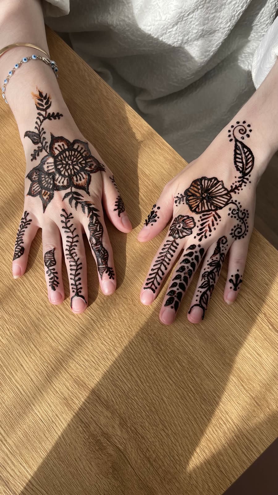 Motifs floraux de henné noir sur les deux mains, sur une table en bois à la lumière du jour