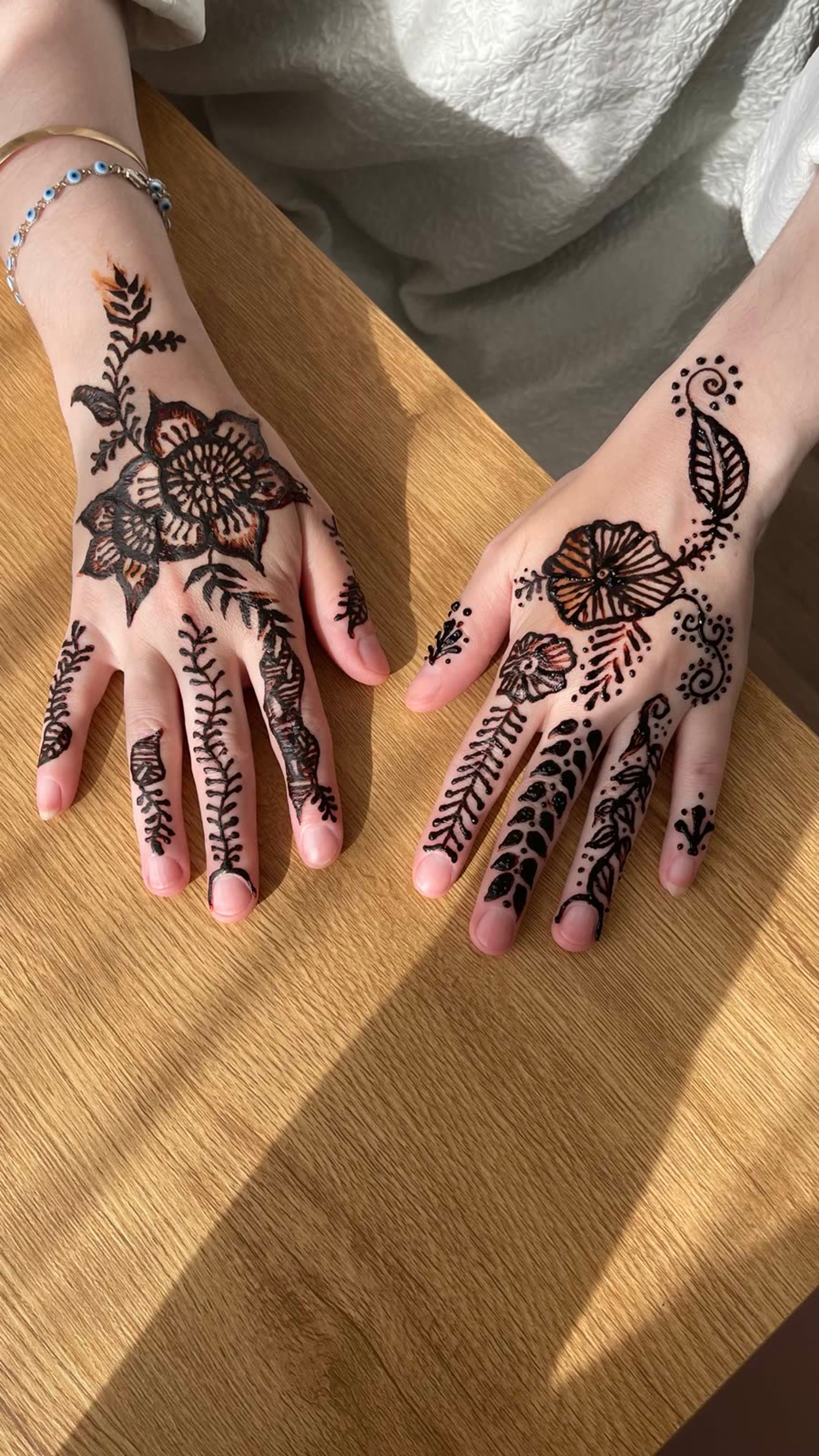 Black henna florals across both hands on a wood table in daylight
