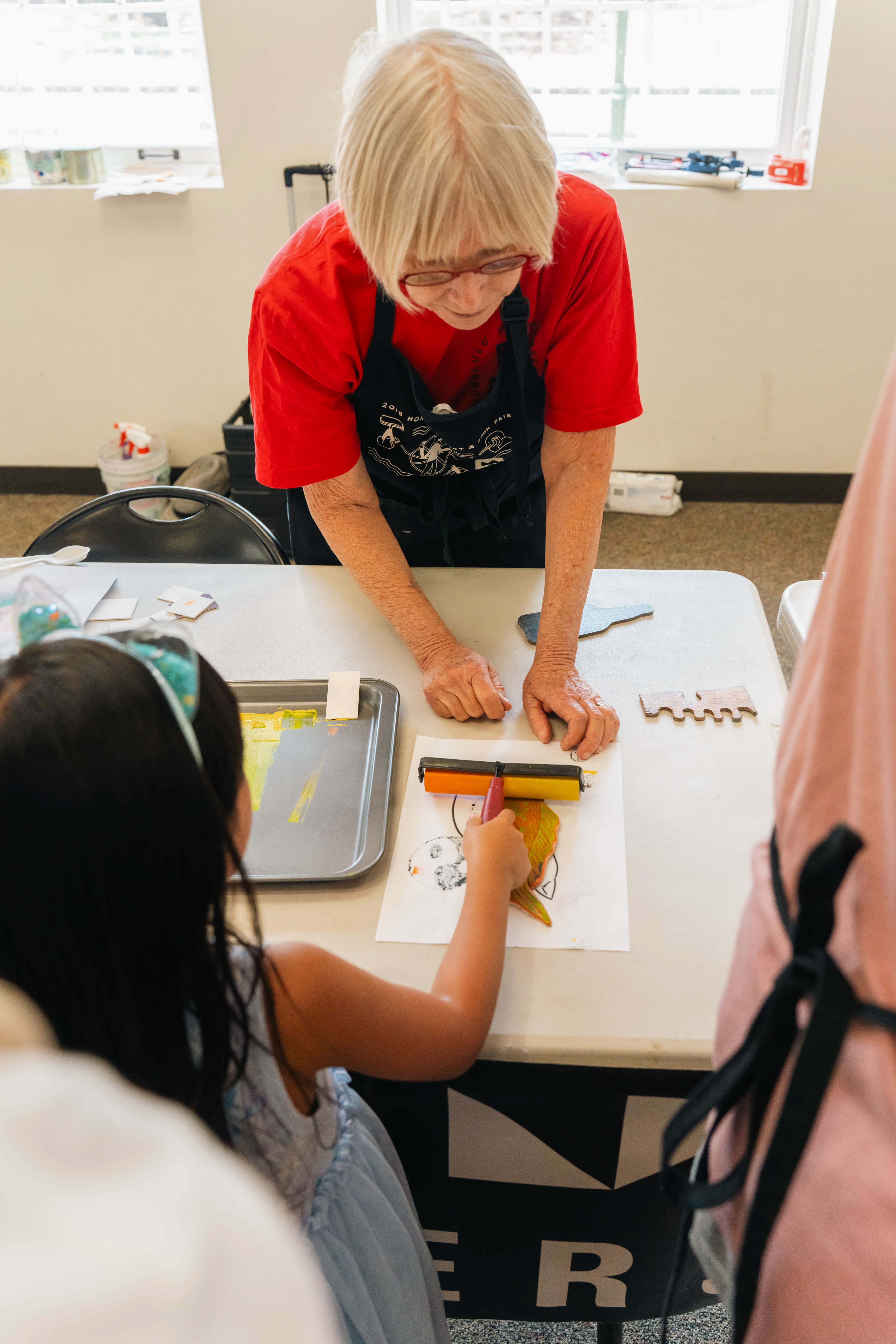 Child rolling ink on to a print block with supervision from a printmaker.