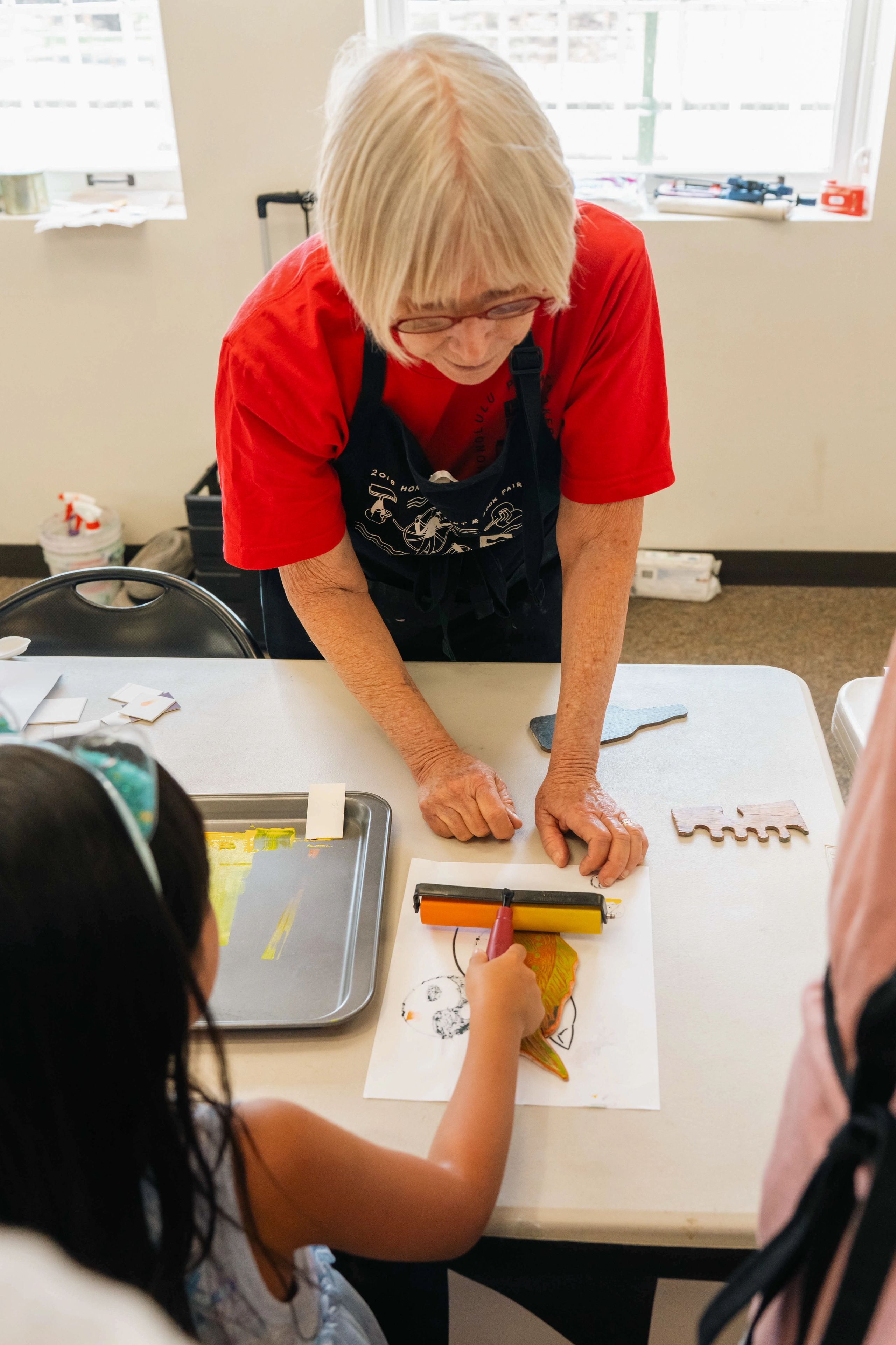 Child rolling ink on to a print block with supervision from a printmaker.