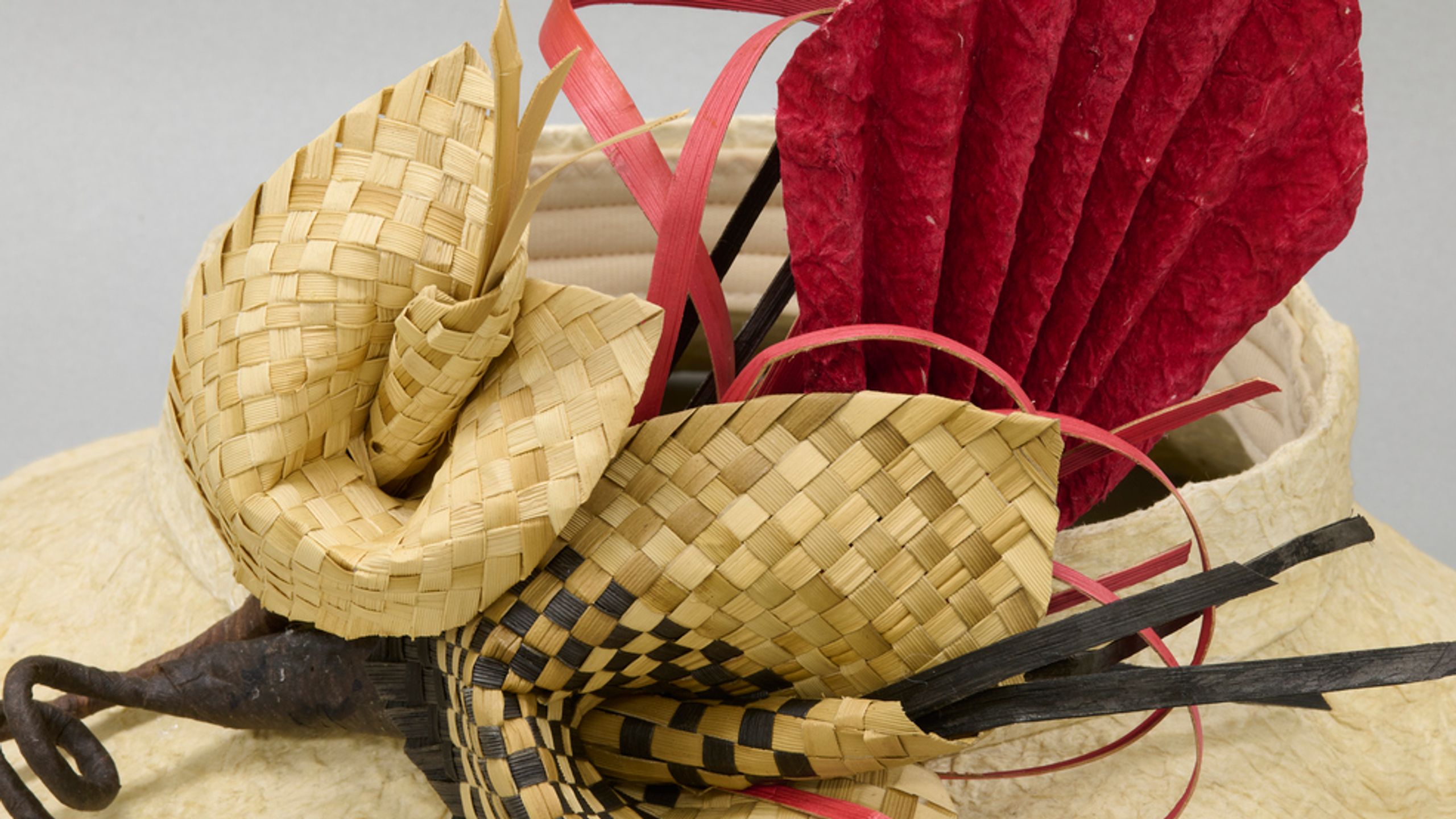 Closeup of open-topped hat made with light brown kapa, decorated with woven flowers.