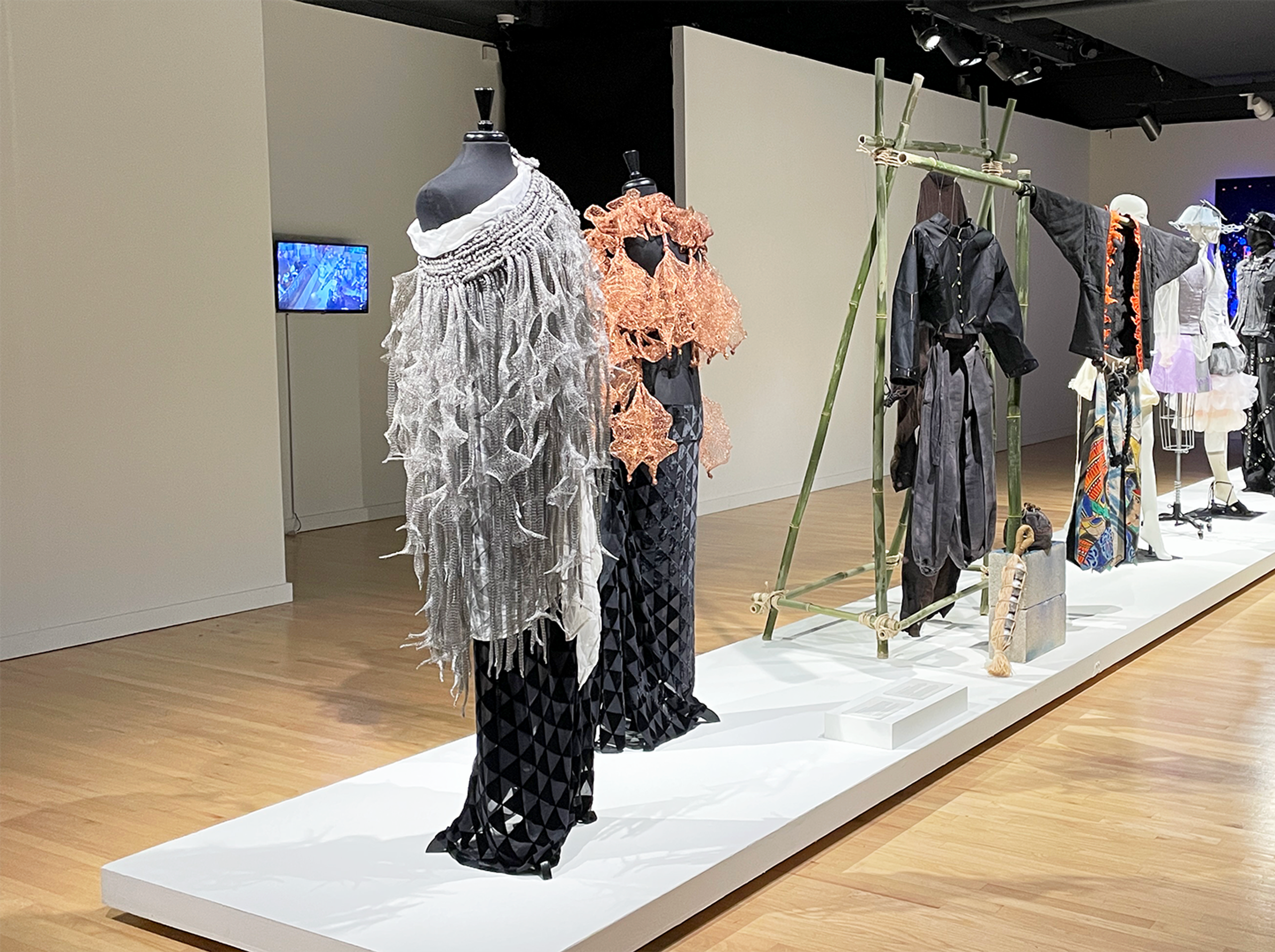 View of gallery with a row of fashion designs on display.