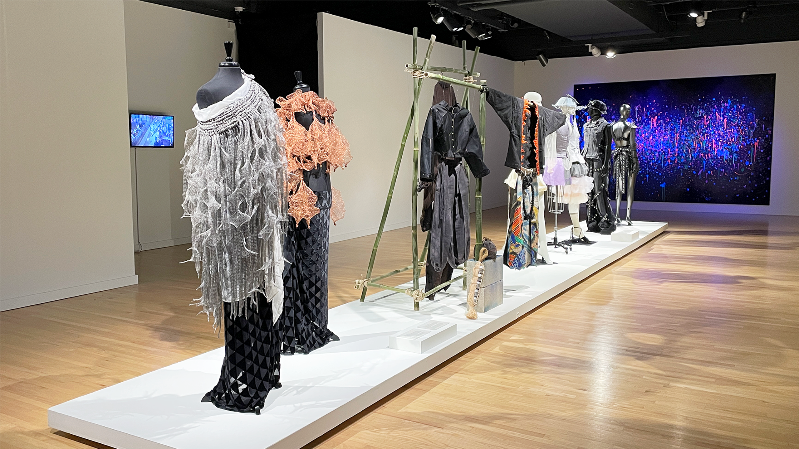 View of gallery with a row of fashion designs on display.