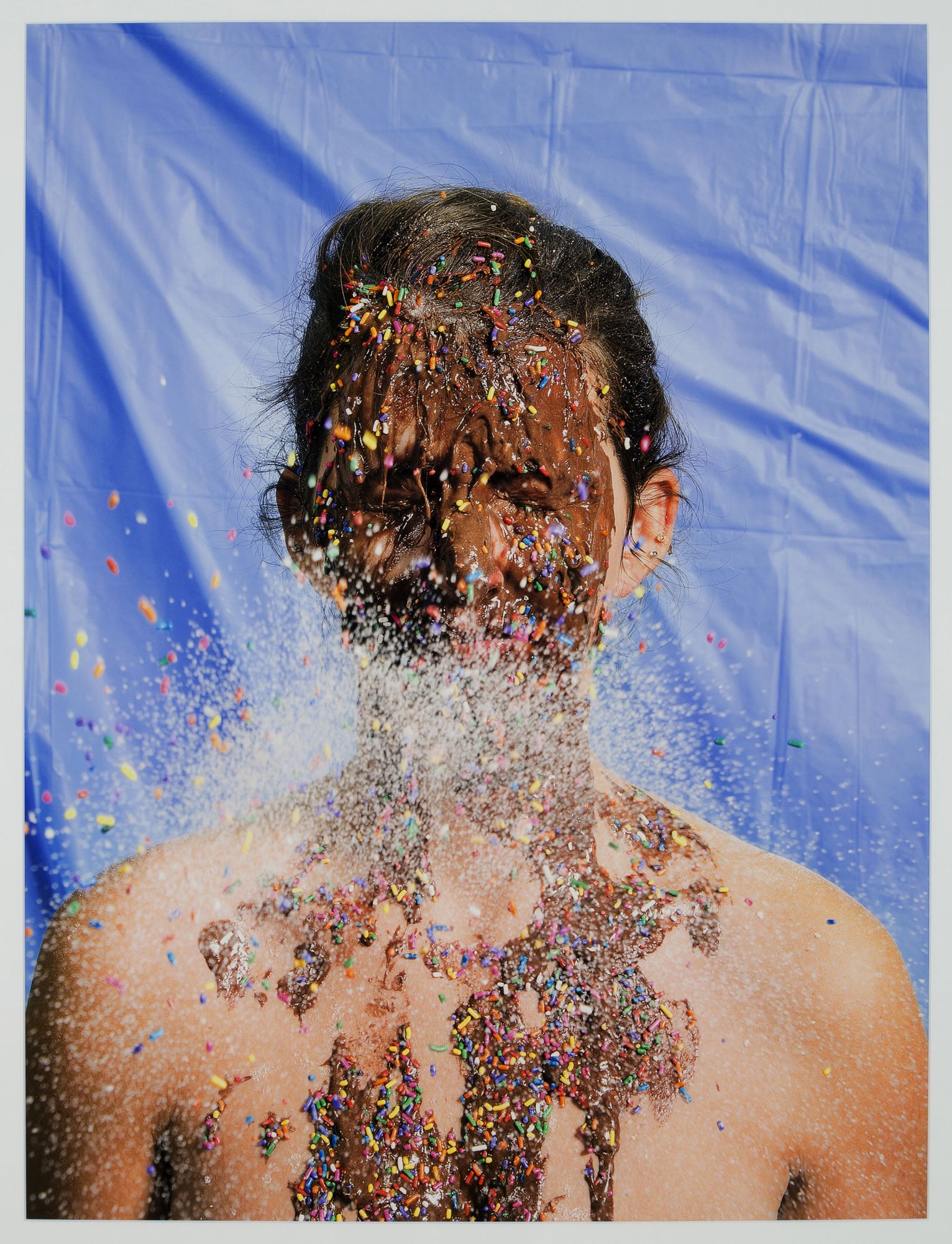 Color photograph of person with chocolate and colorful candy sprinkles on their face and upper chest.