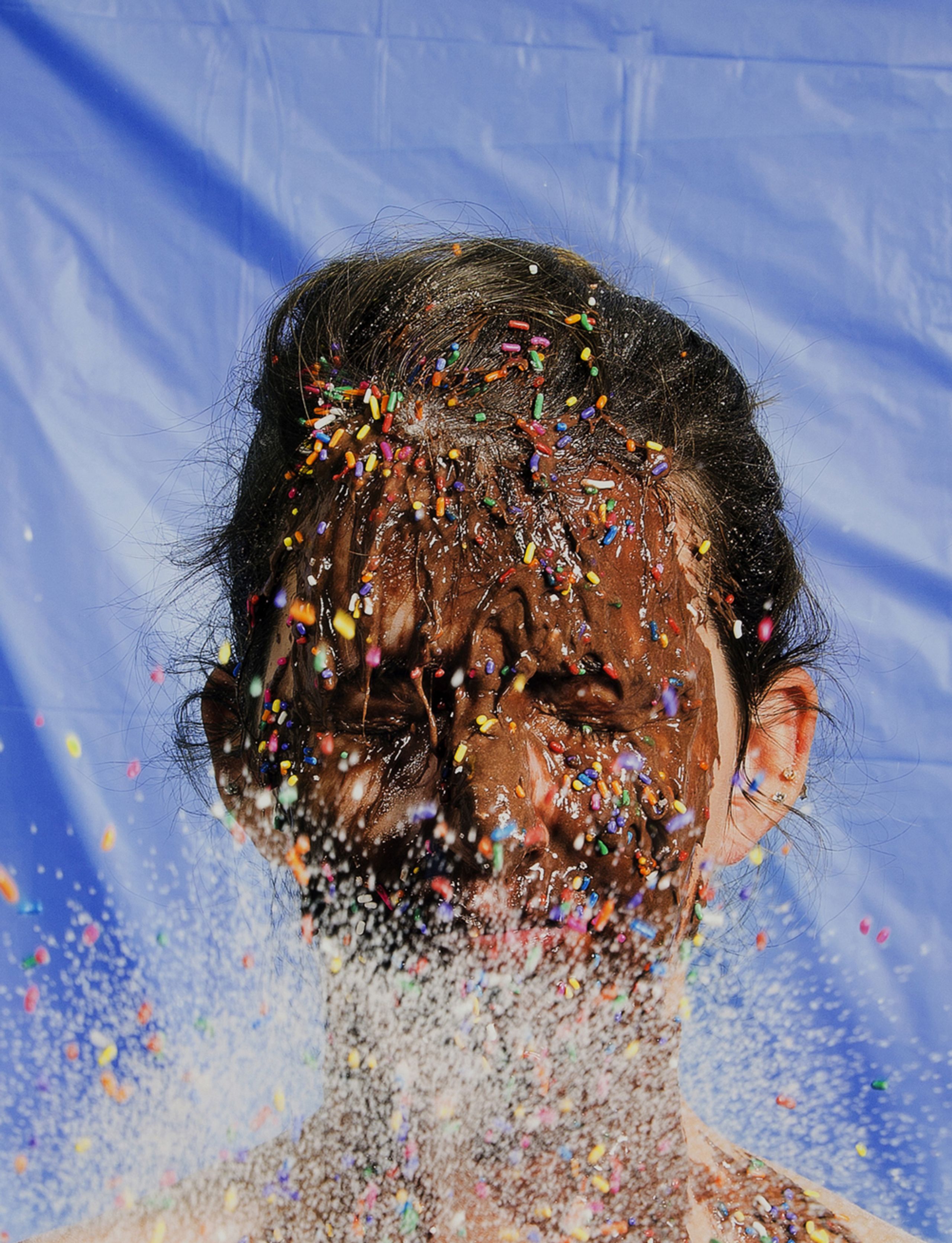 Color photograph of person with chocolate and colorful candy sprinkles on their face and upper chest.