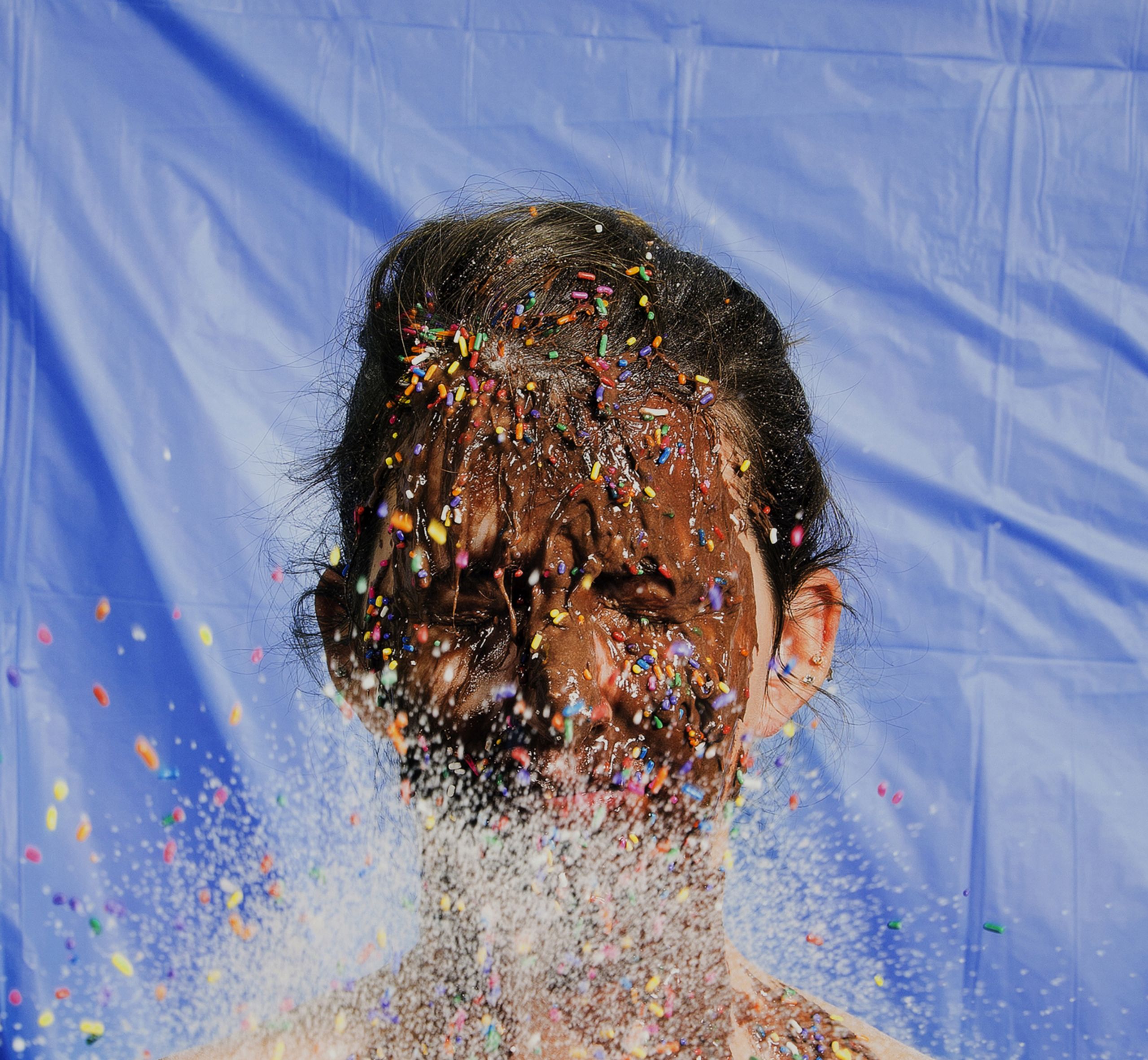 Color photograph of person with chocolate and colorful candy sprinkles on their face and upper chest.