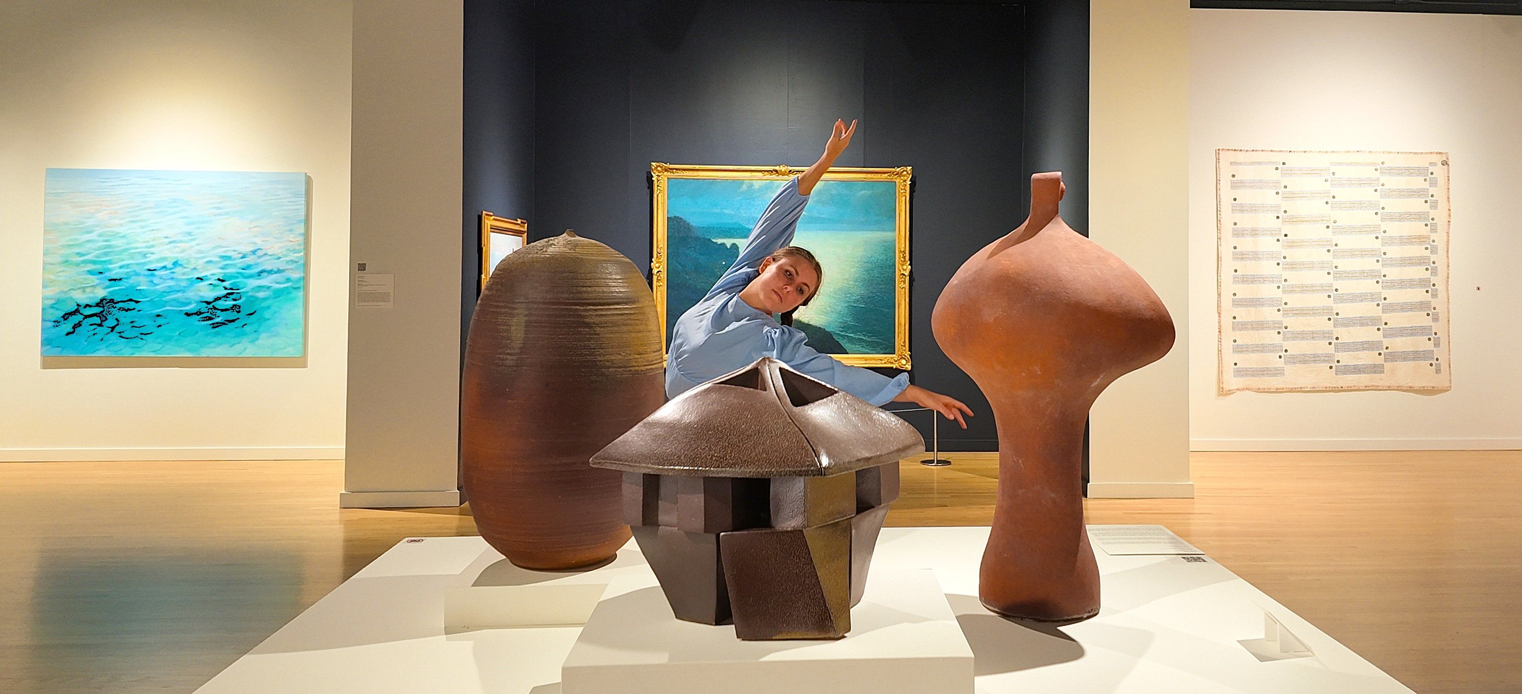 Dancer with arms up, behind a display table of sculptures.
