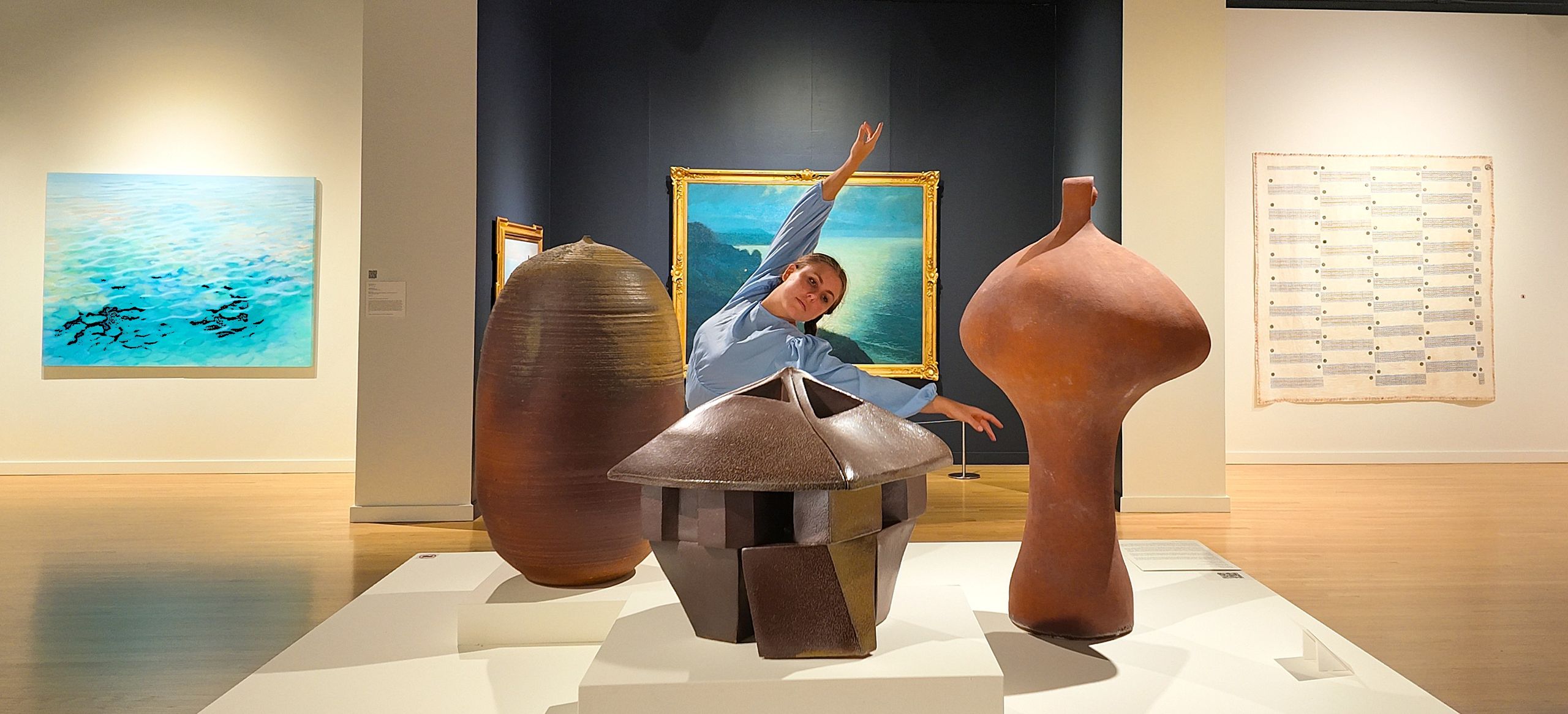 Dancer with arms up, behind a display table of sculptures.