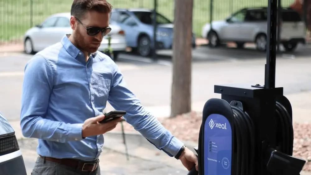 a man is charging his electric car at a charging station while looking at his phone .