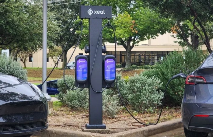 two electric cars are being charged at a xeal charging station in a parking lot .