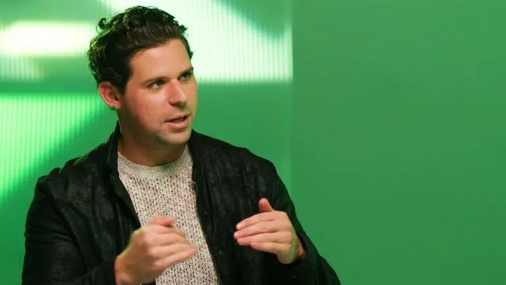 a man is sitting in front of a green wall talking to someone .