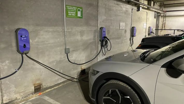 two electric cars are being charged at charging stations in a parking garage .