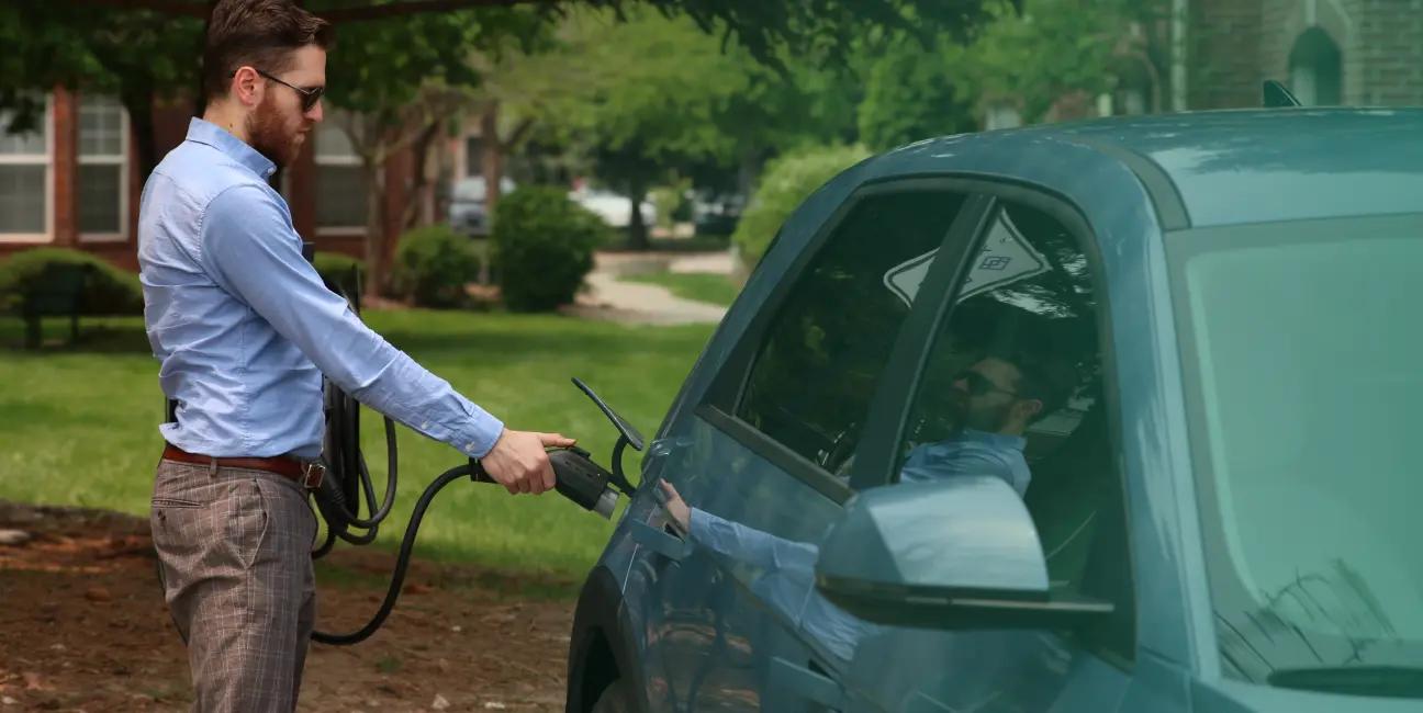 a man is charging his electric car in his driveway .