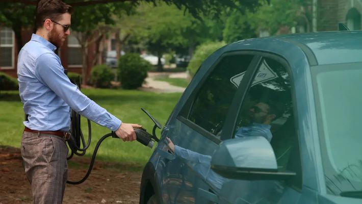a man is charging his electric car in his driveway .