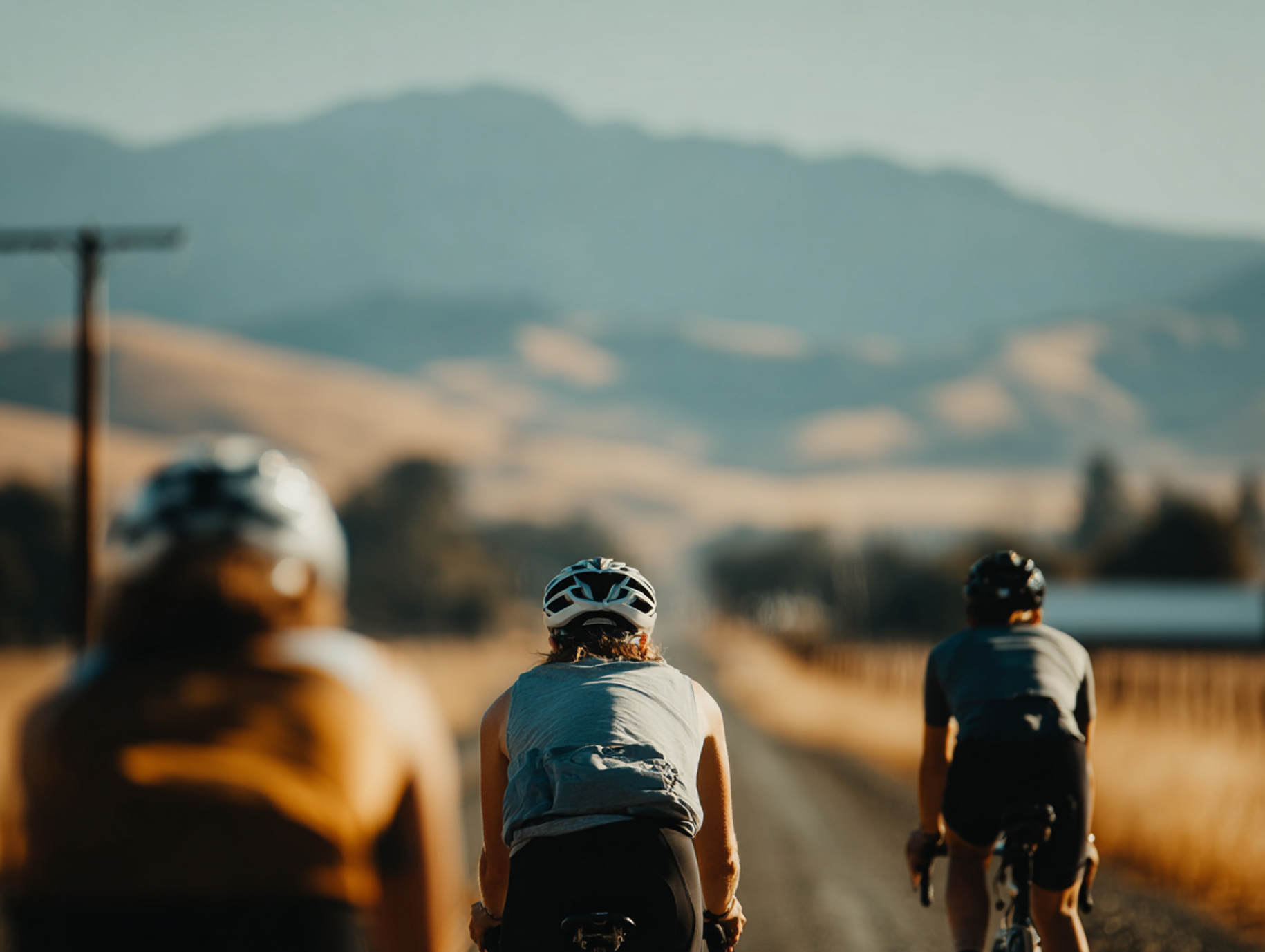 Group of 3 bikers riding away on gravel road in hilly area