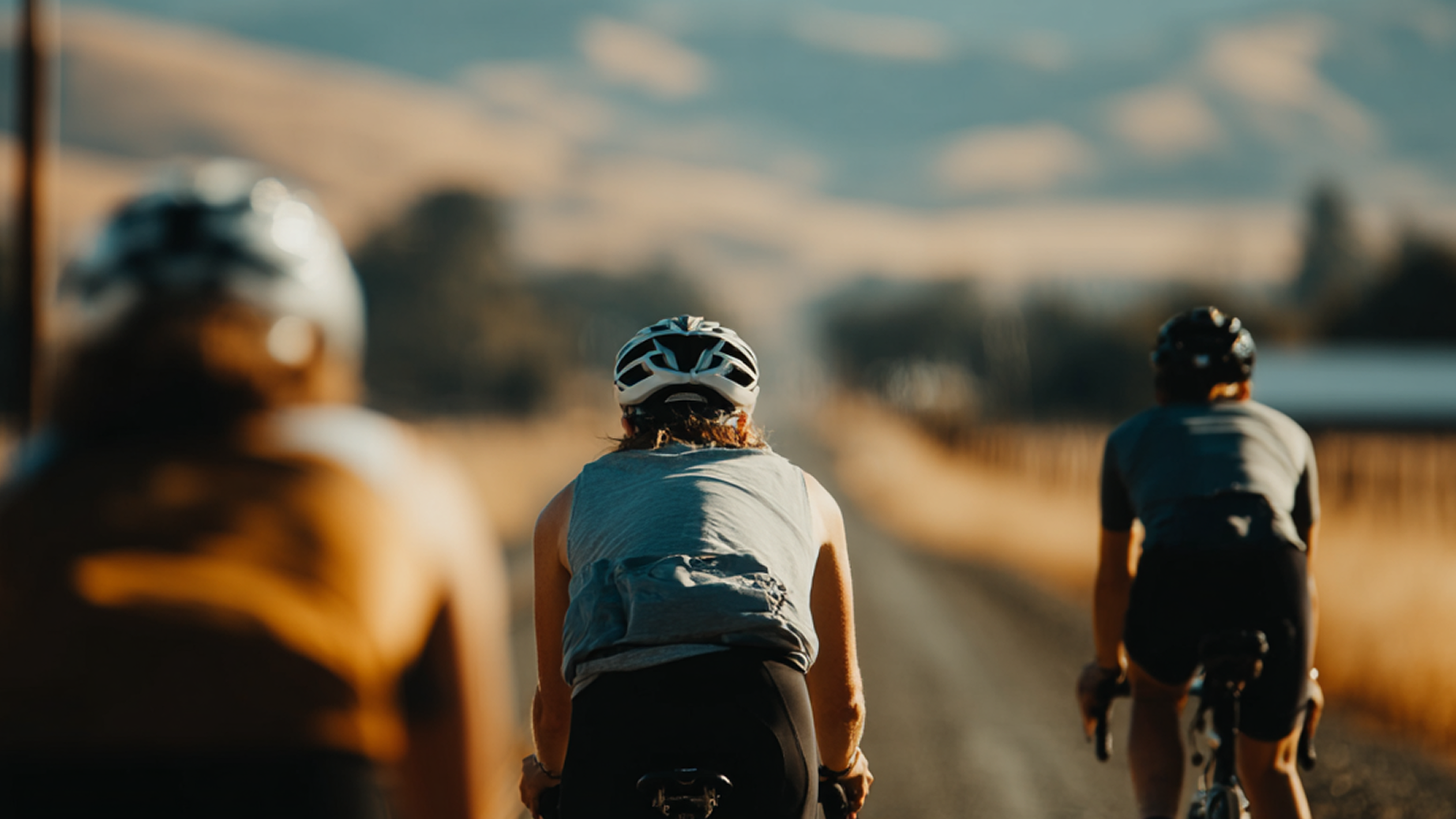 Group of 3 bikers riding away on gravel road in hilly area