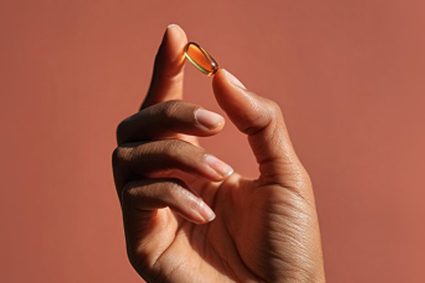 Hand holding pill in between fingers on plain background