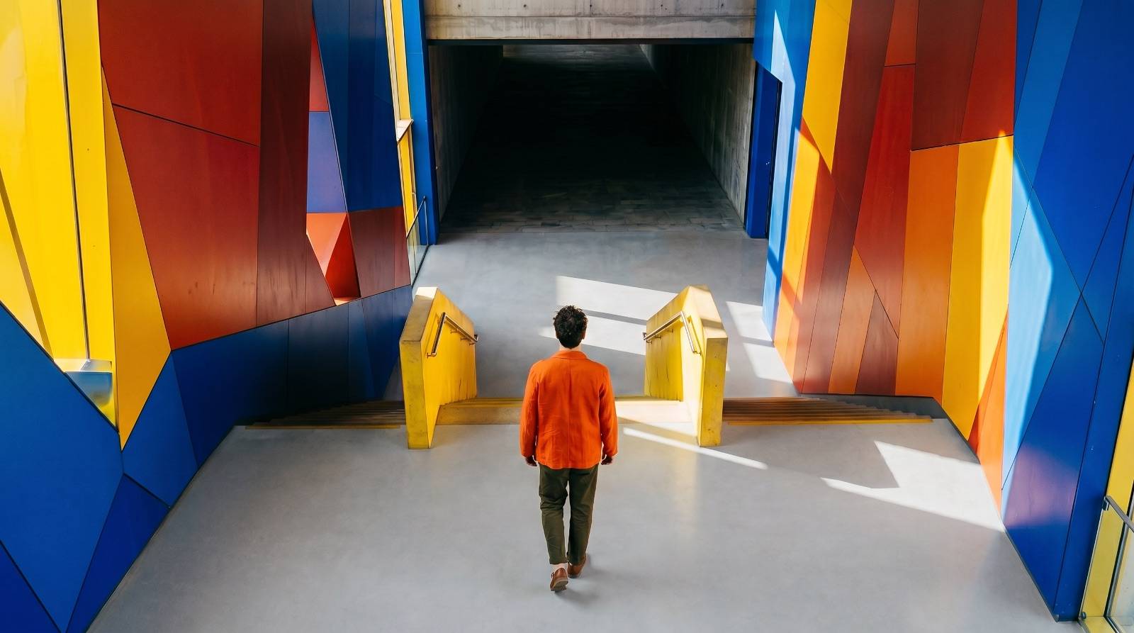 An architectural threshold where a dark, low space opens suddenly into bright colour and height.