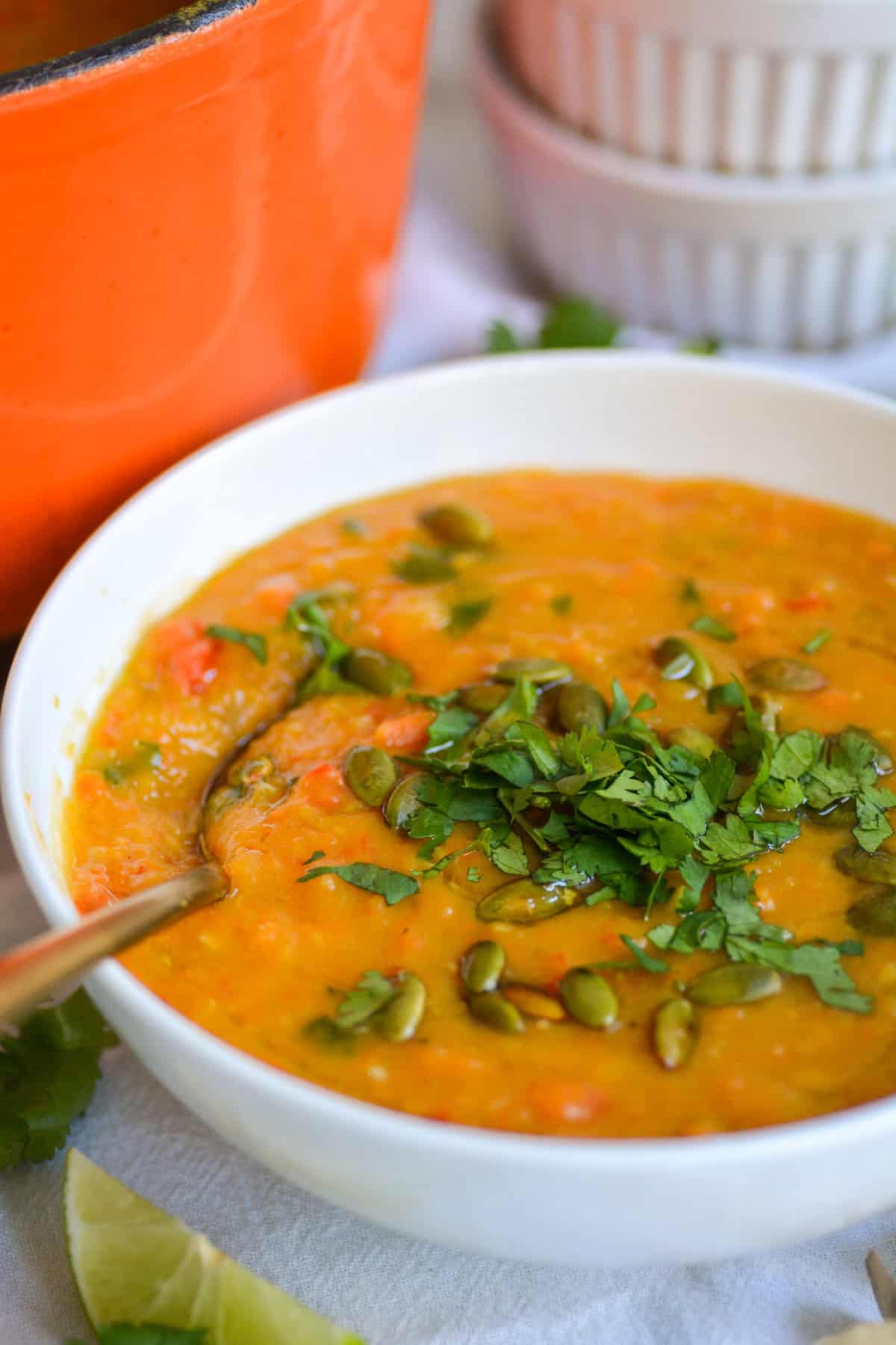 A bowl of carrot red lentil soup with a spoon, topped with chopped herbs. 