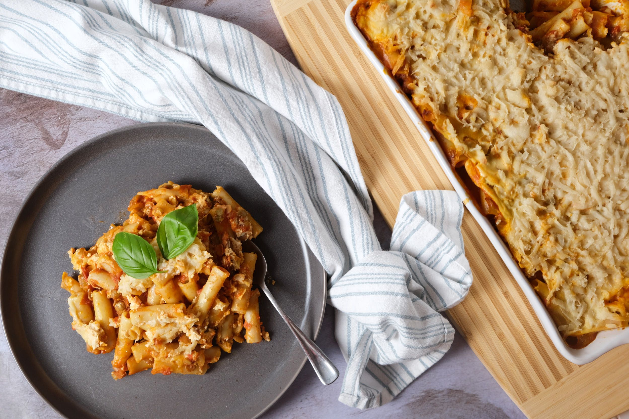 top down view of baked ziti on plate with the casserole to the right on a cutting board