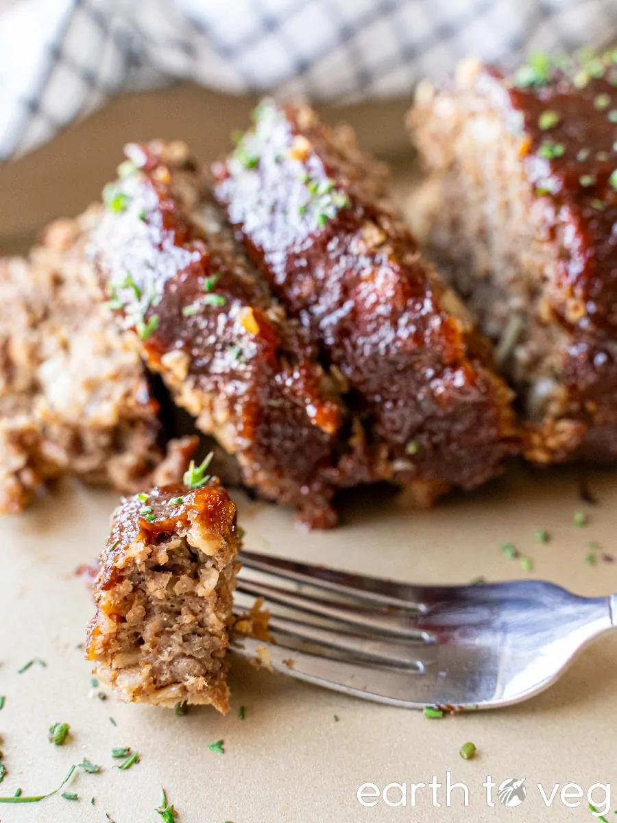 Slices of Impossible meatloaf behind a piece of Impossible meatloaf on a fork.