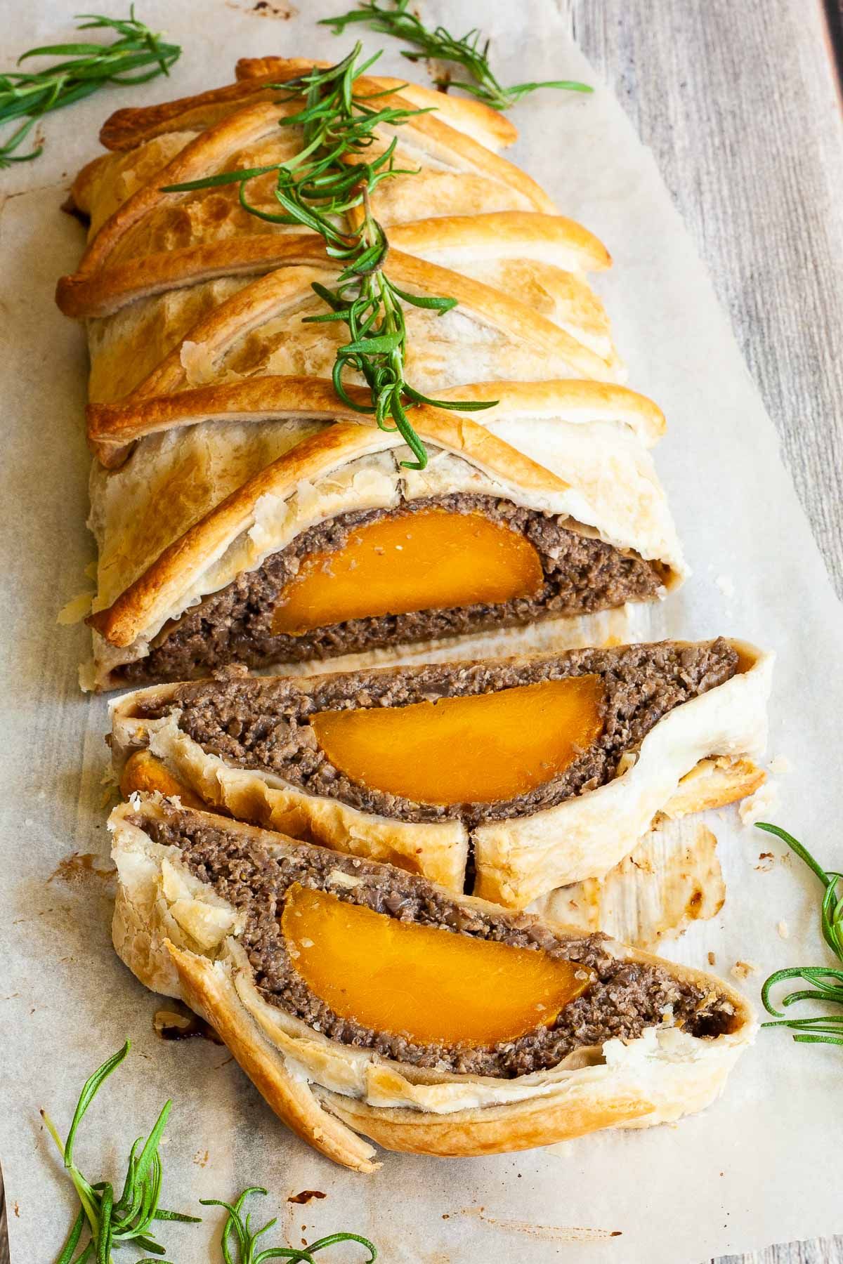 A vegan butternut squash Wellington on a piece of parchment, sliced, and topped with rosemary. 