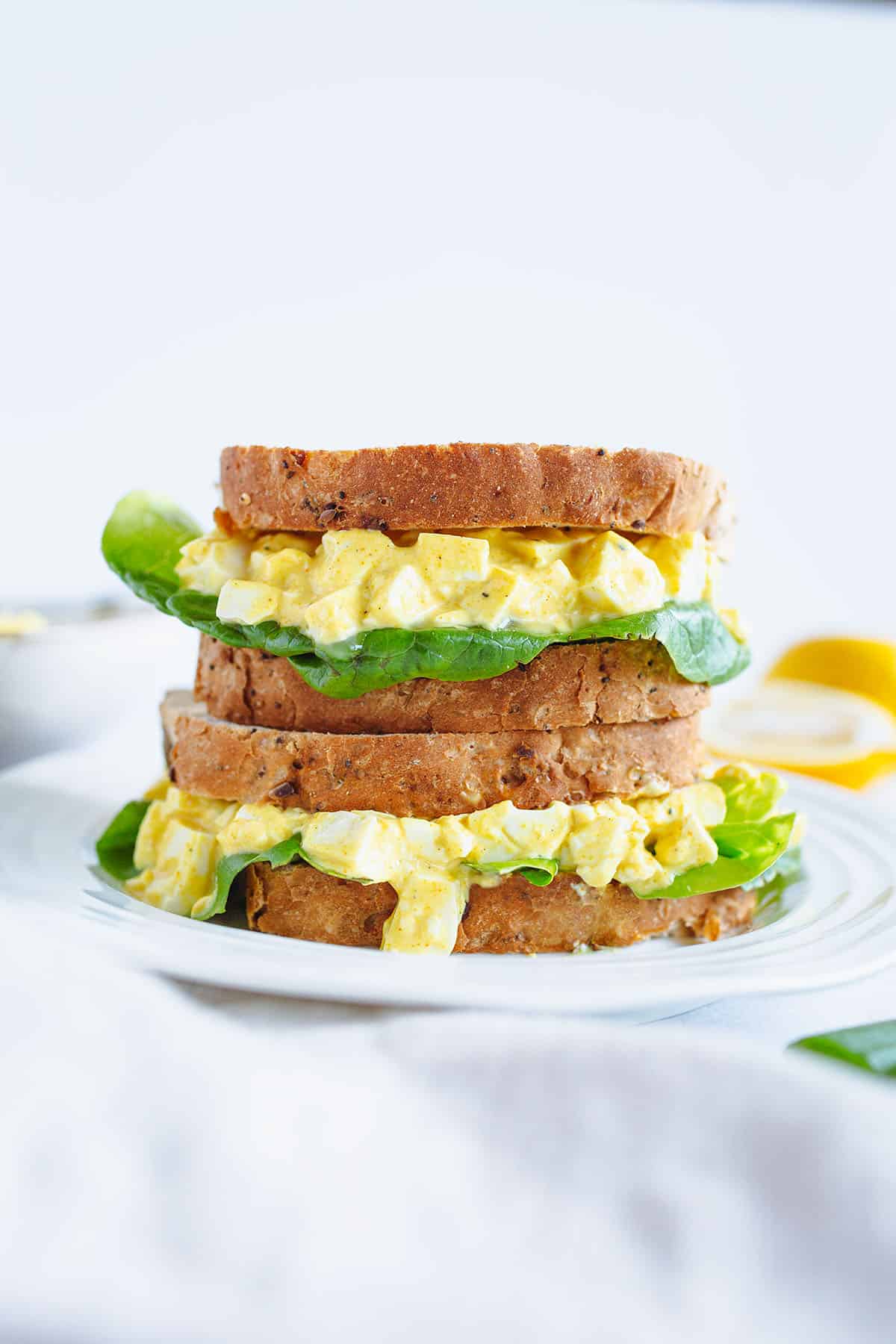 Two vegan egg salad sandwiches stacked on a plate. 