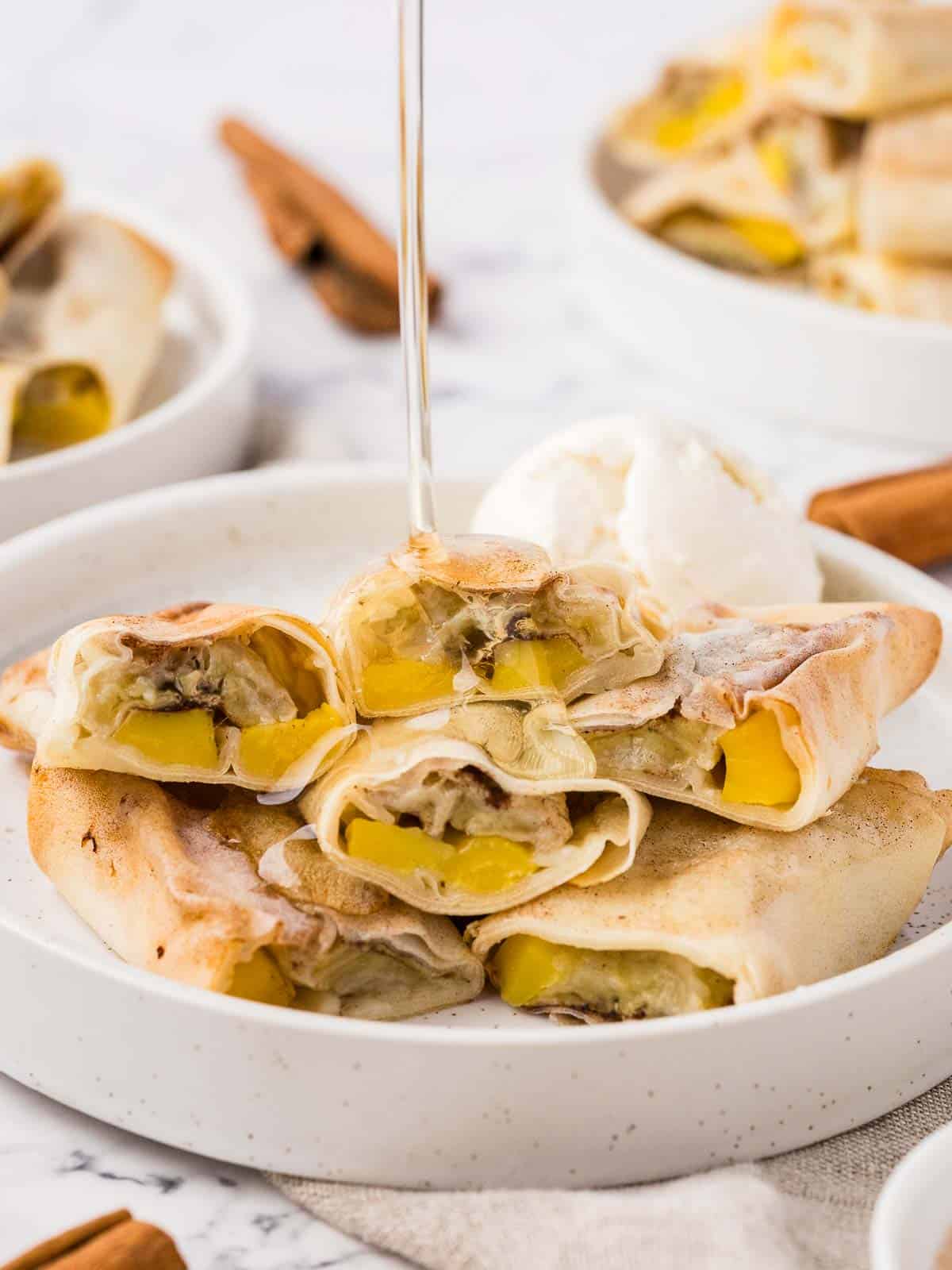 A plate of banana spring rolls with a sweet sauce being drizzled on top. 