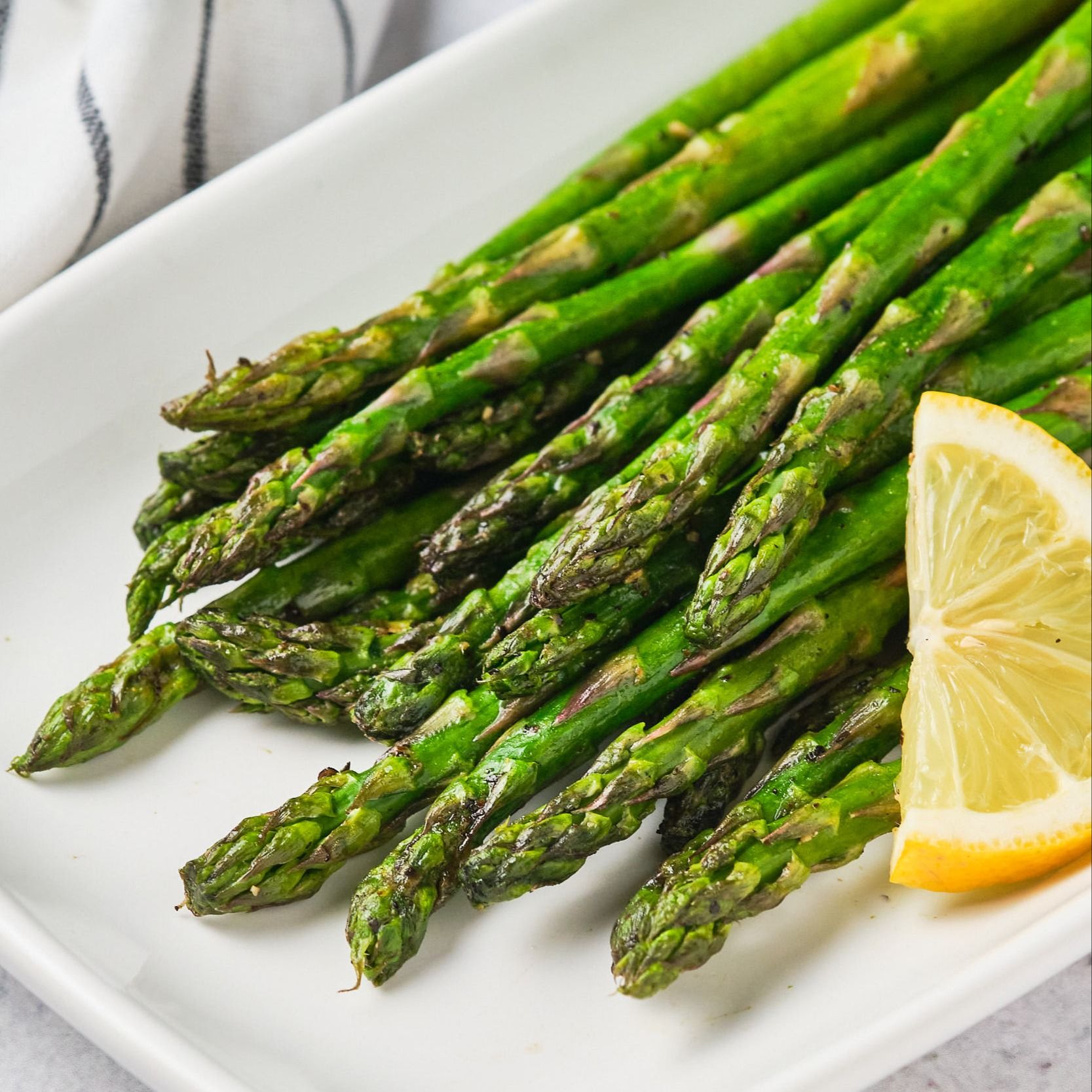 Air fryer asparagus on a platter with a lemon slice.