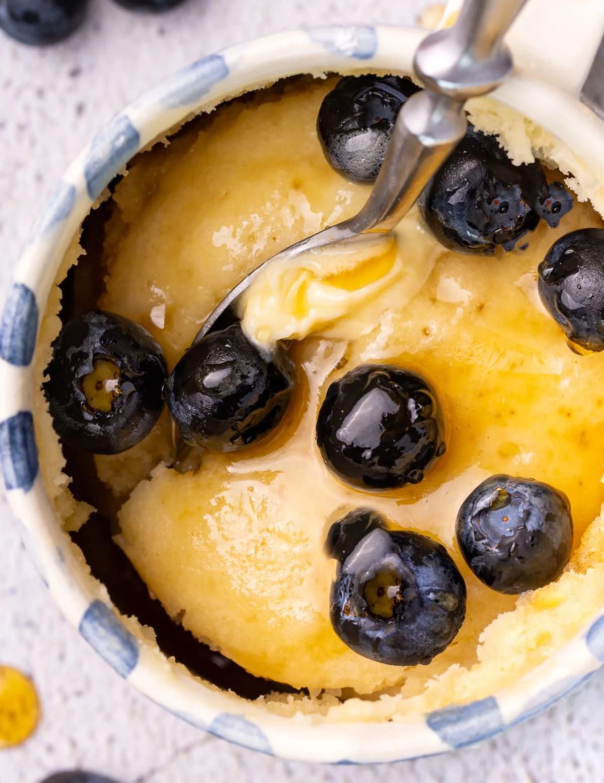 A pancake in a mug with a spoon and blueberries. 